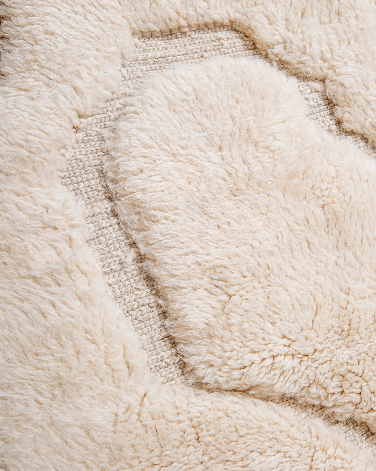 Close up of cream wool rug with design made of thickly knotted and flat woven areas.