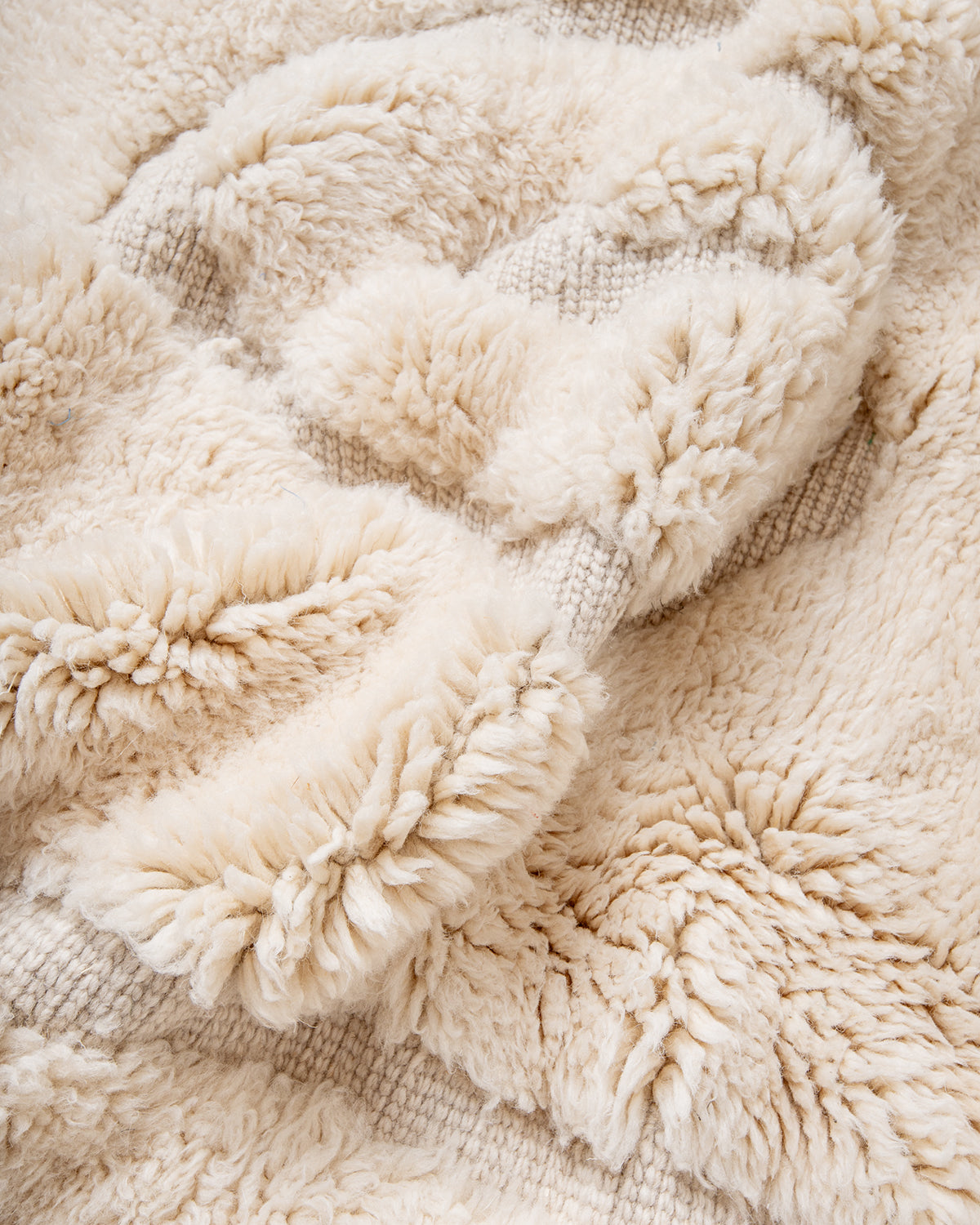 Thick fluffy wool of cream M'rirt rug bunched up to show velvety texture.
