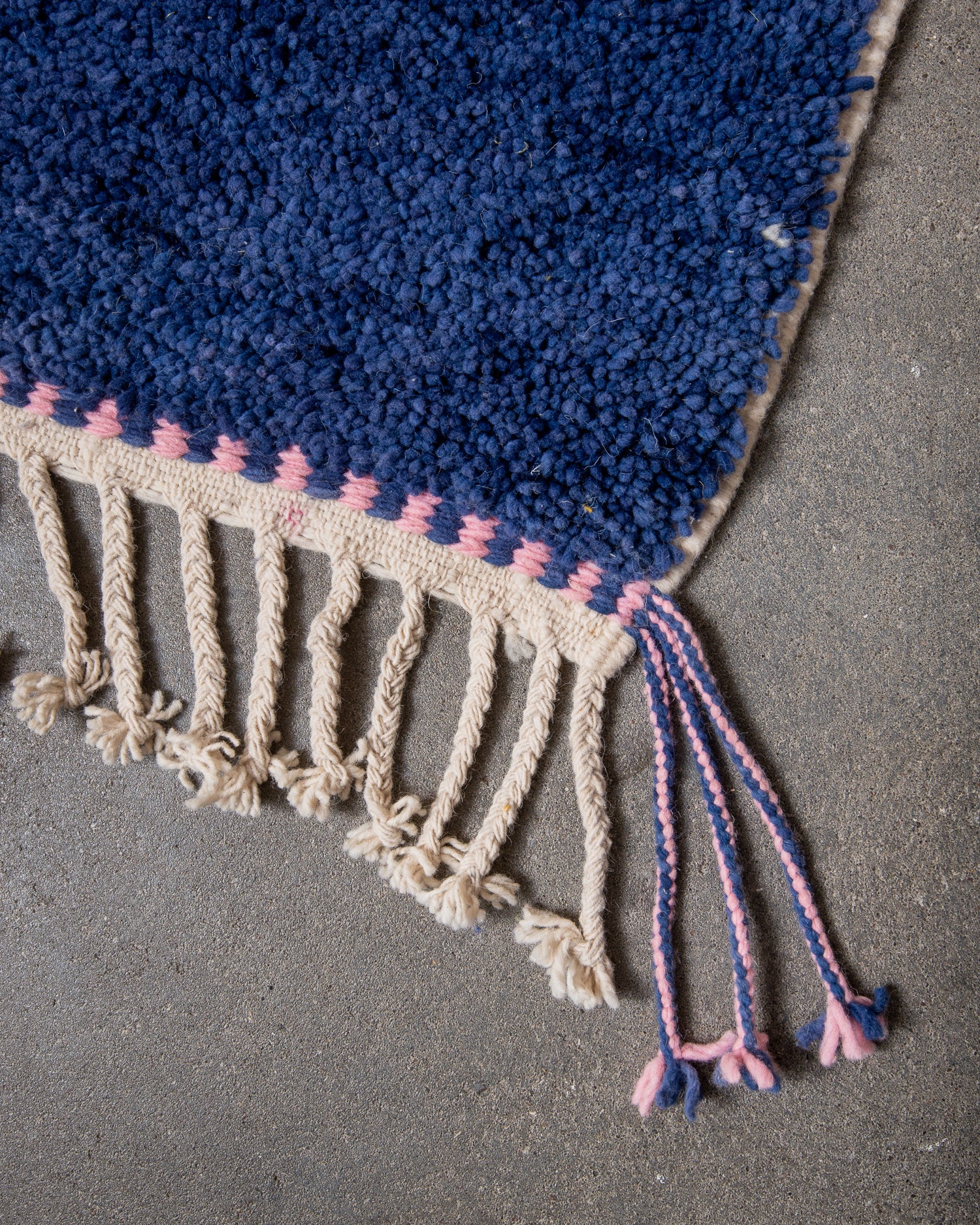 Corner of beniourain rug with natural wool tassels along the end and pink and blue tassels at the corner.