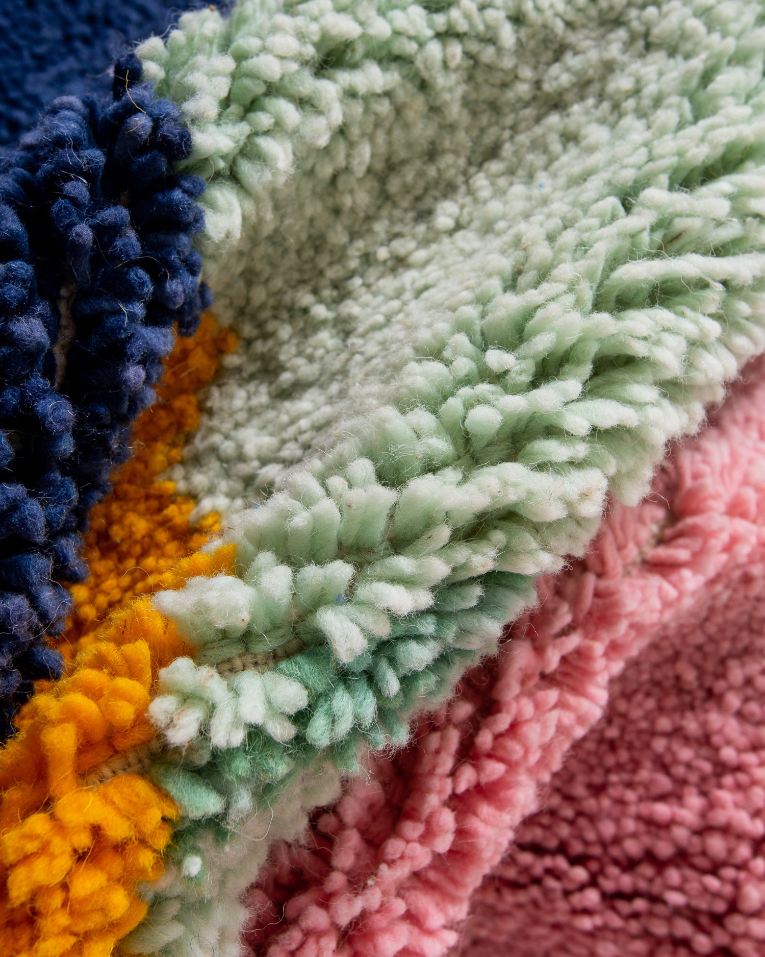 Close up of texture of Beniourain rug made of fluffy wool in mint green, navy blue, egg yolk yellow and rose pink.