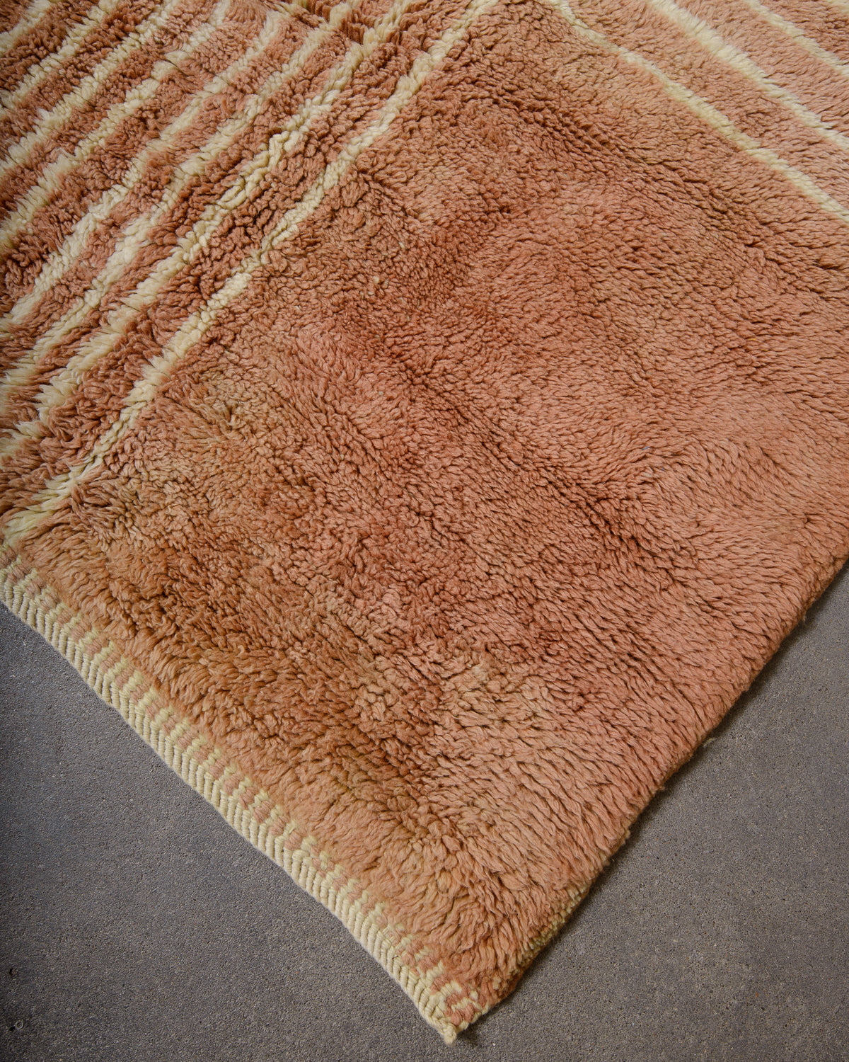 Corner of Beni M'rirt rug in camel brown and lemon cream wool showing its woven edge laying on concrete studio floor.