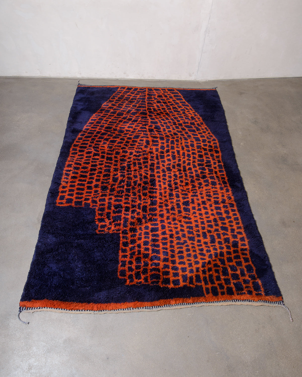 Beni M'rirt rug from Morocco in deep navy blue with contrasting rust red abstract grid pattern laying on concrete studio floor.