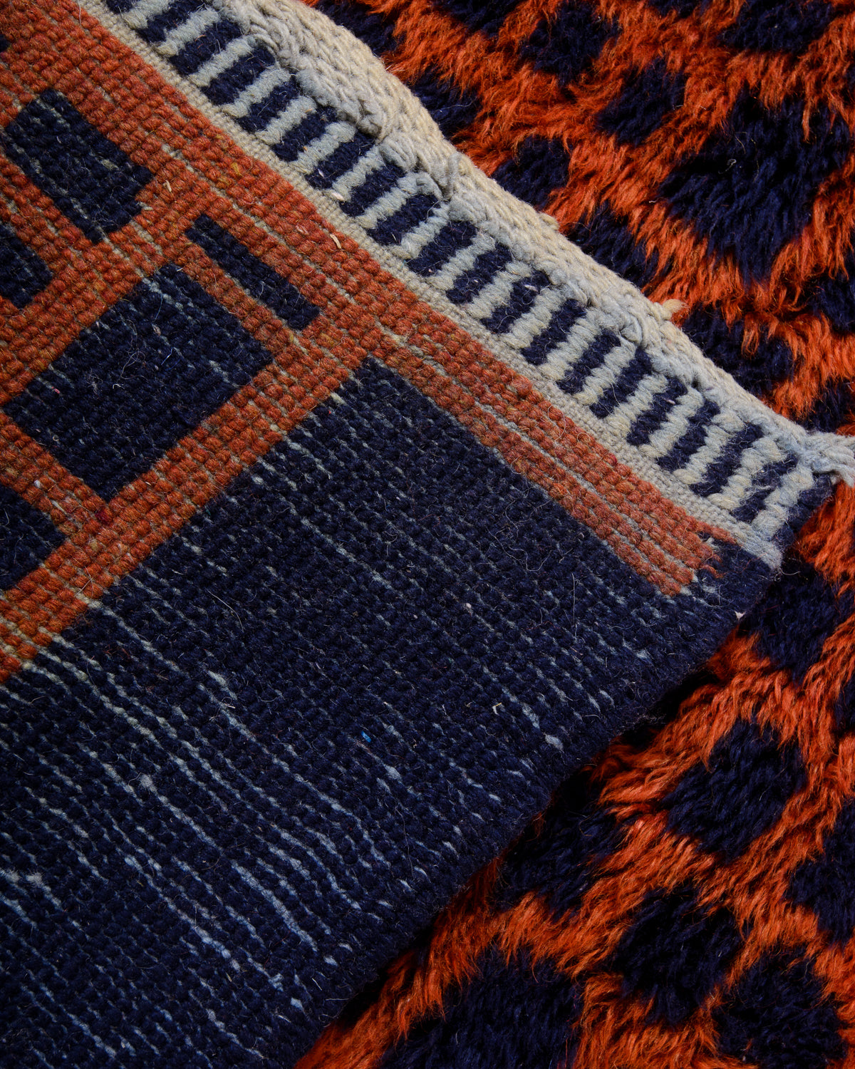 Back corner of Beni M'rirt rug in dark navy, rust red, light blue and cream showing density of knots.