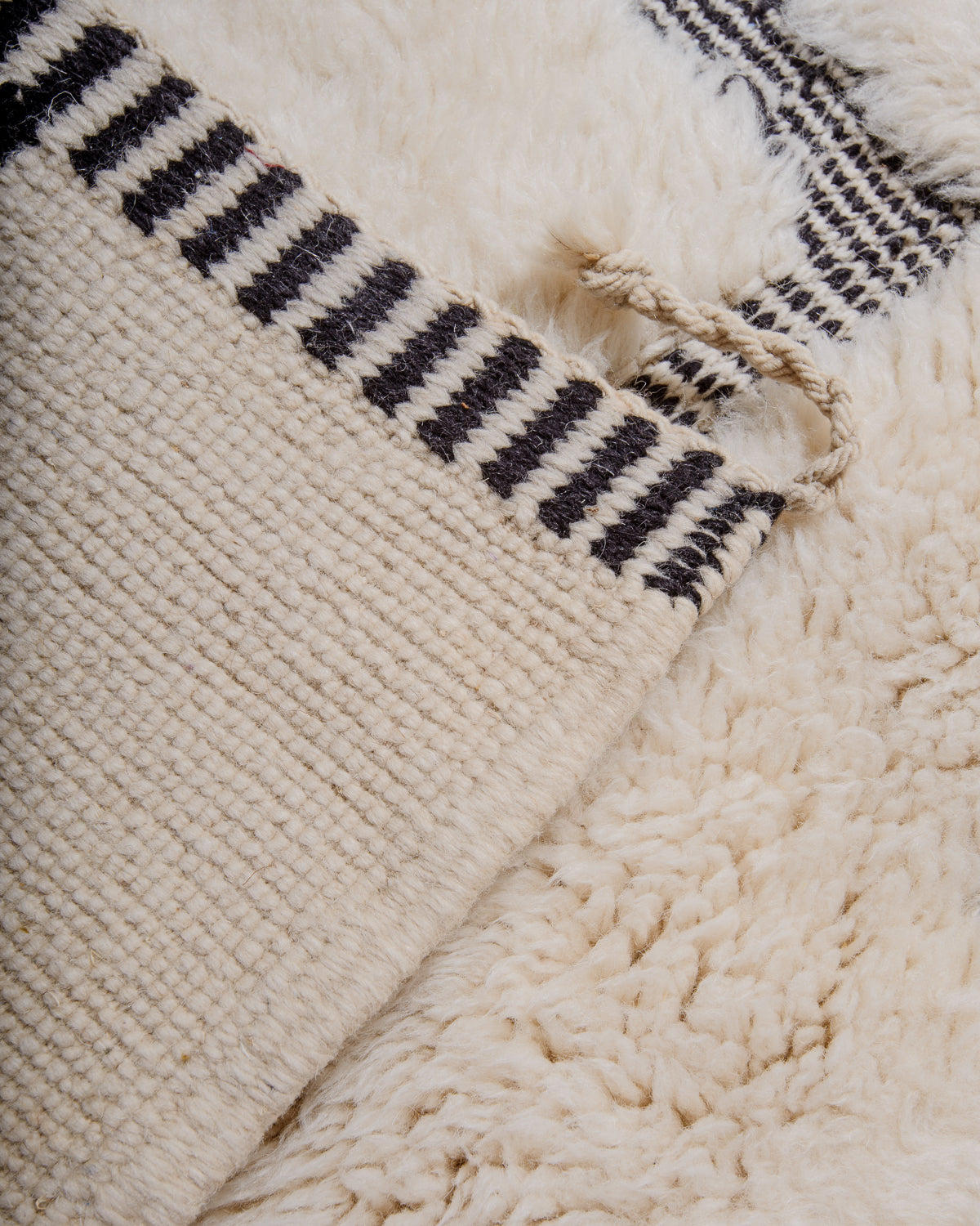 Back corner of Beni M'rirt rug showing number of knotted rows in cream wool with black and white design.