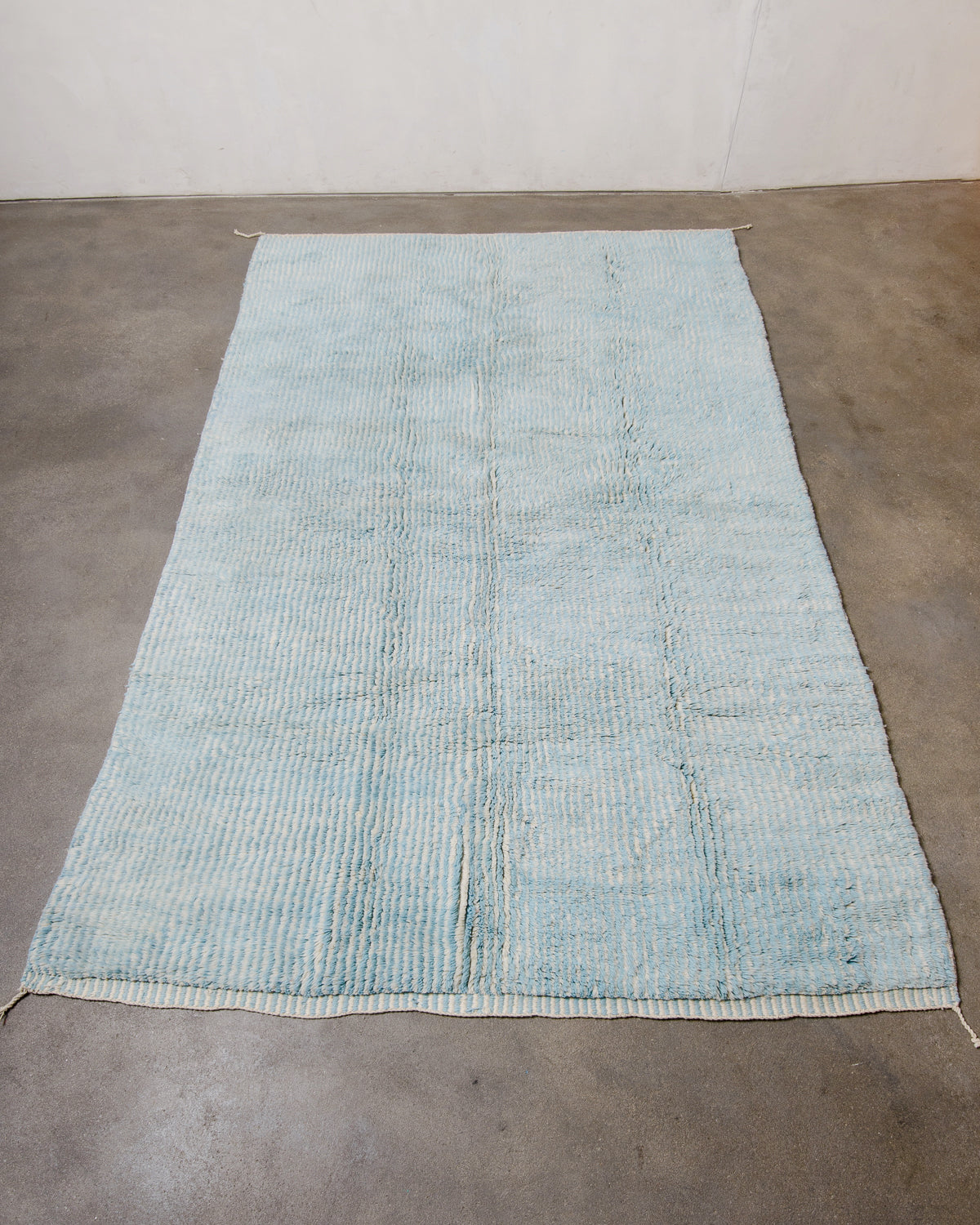 Wool Beni M'rirt rug in cream and light blue stripes laying on concrete floor of studio.