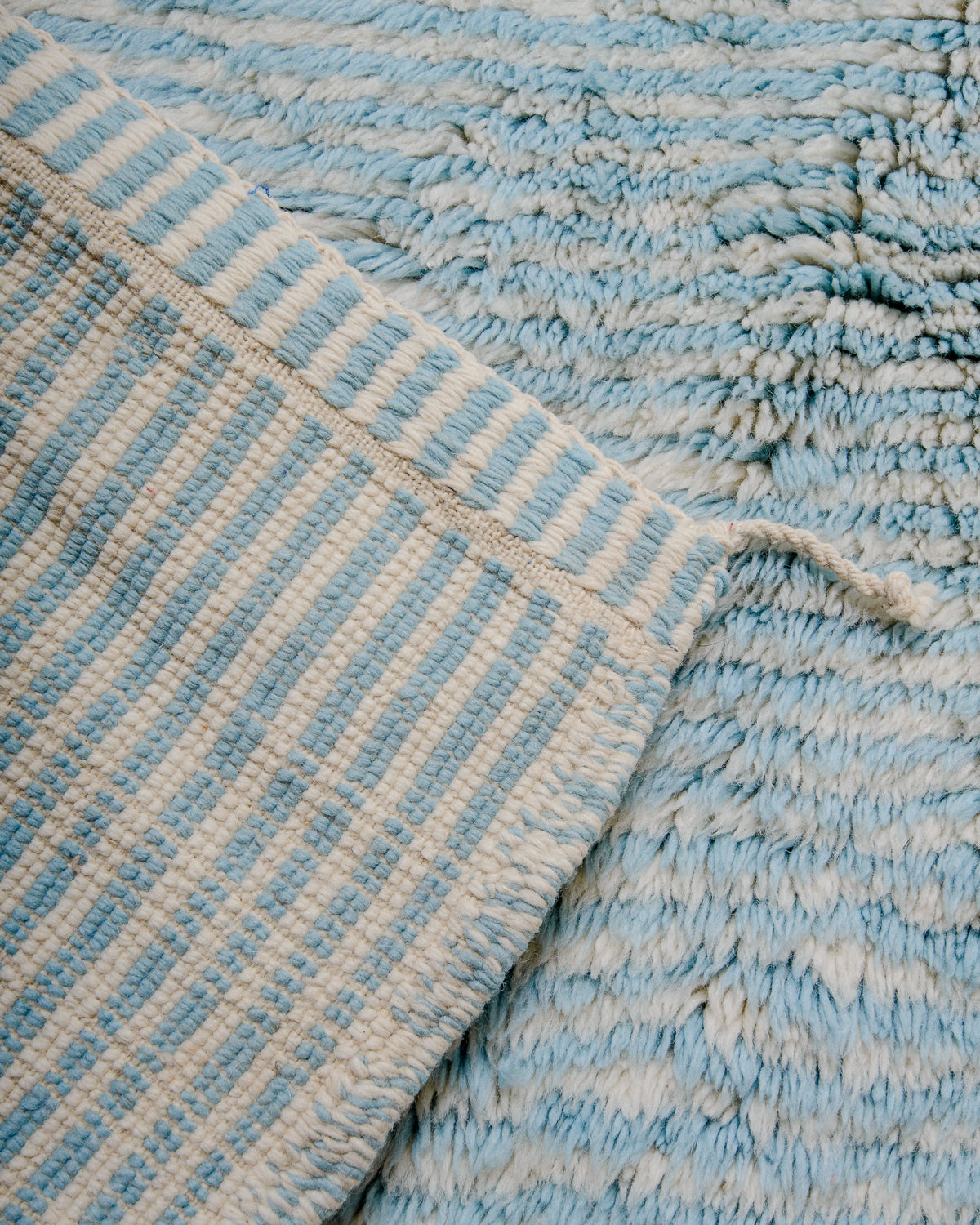 Corner of Beni M'rirt rug in cream and light blue stripes showing the number of knots on the back of the rug.