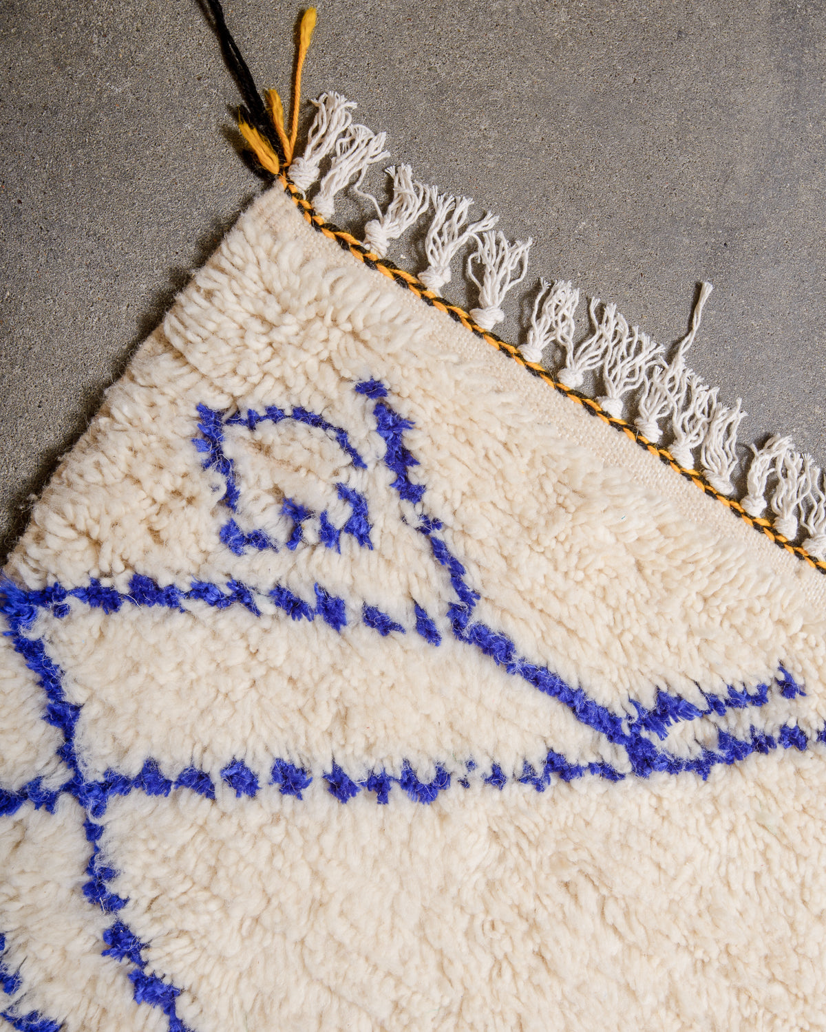 Cotton tassels on edge of cream wool Azilal rug with black and yellow edge.