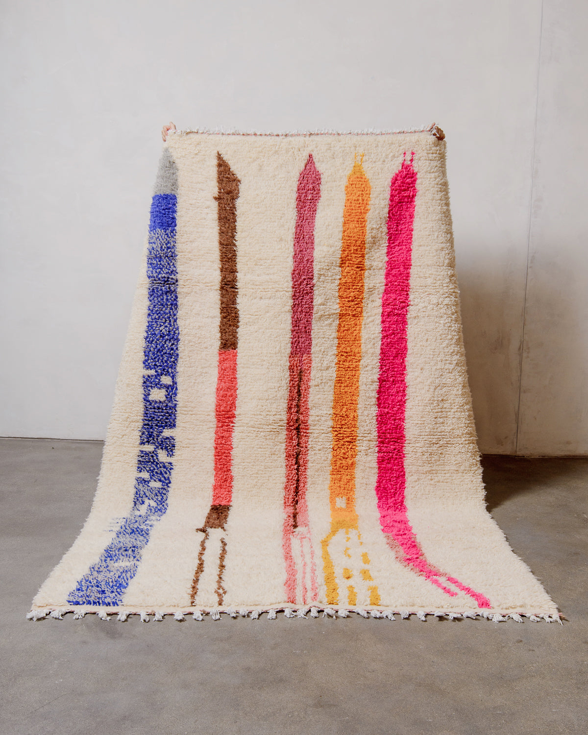 Berberlin Azilal rug made of sheep’s wool being held up against a white studio wall.