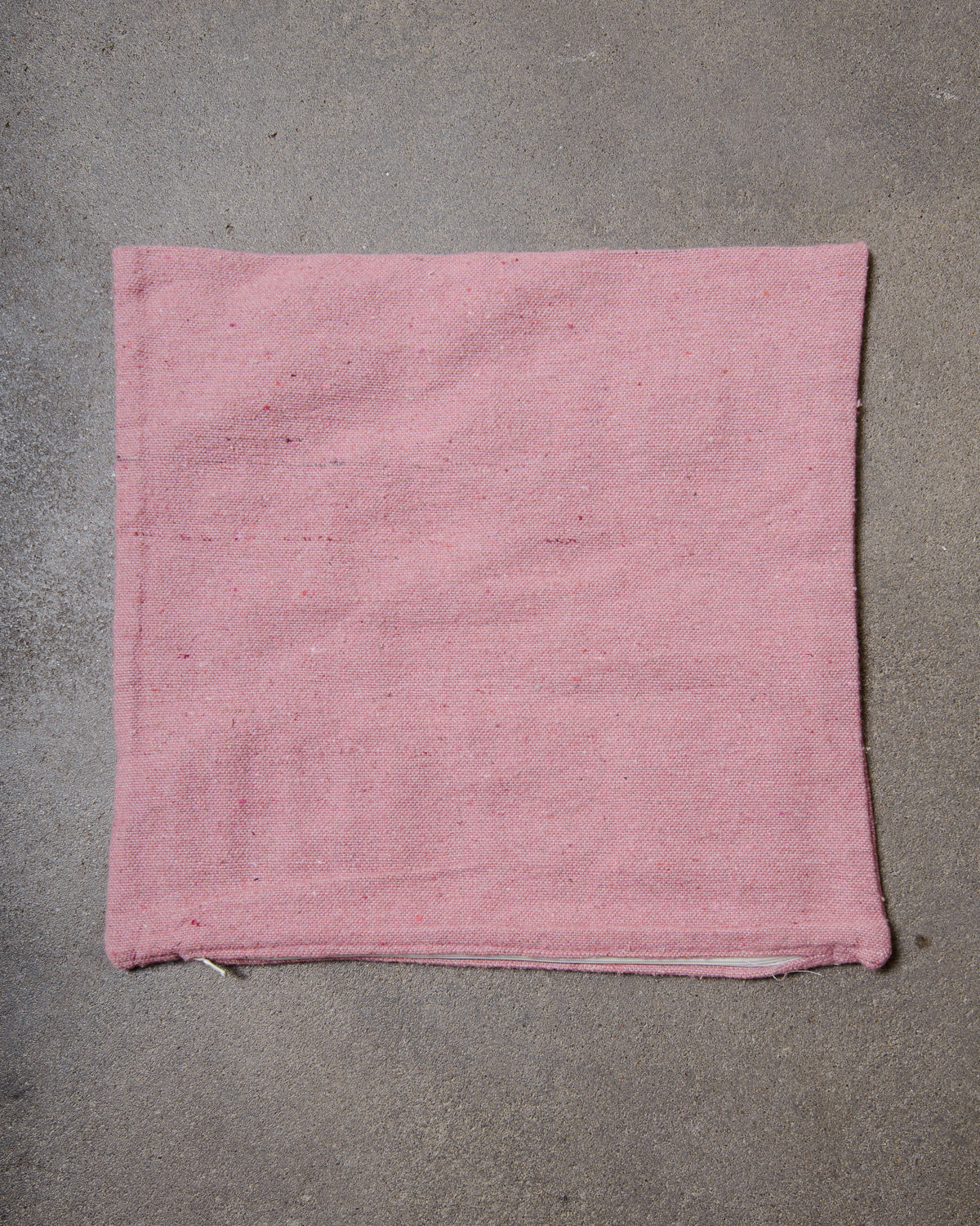 Back of pink wool cushion cover with white zip, laying on concrete studio floor.