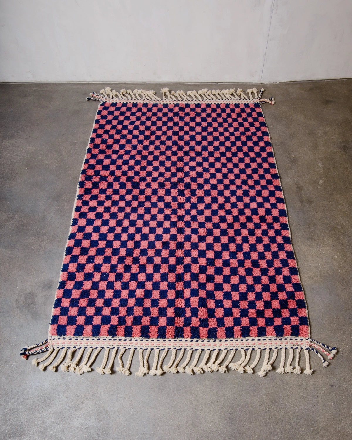 Beniourain rug with a navy and dark pink checkered pattern laying flat on concrete studio floor.