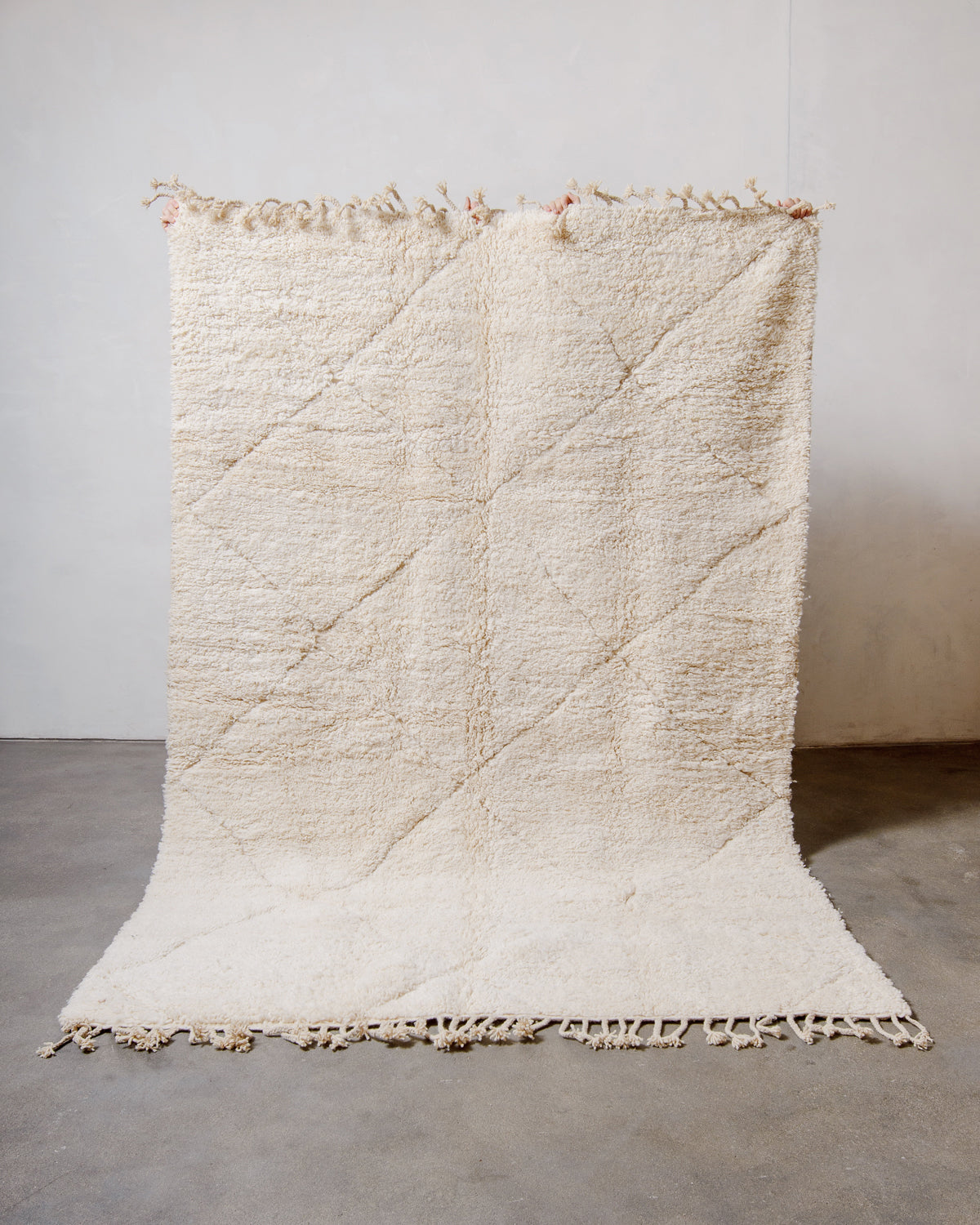 Berberlin Beniourain rug made of sheep's wool held up against white wall. 