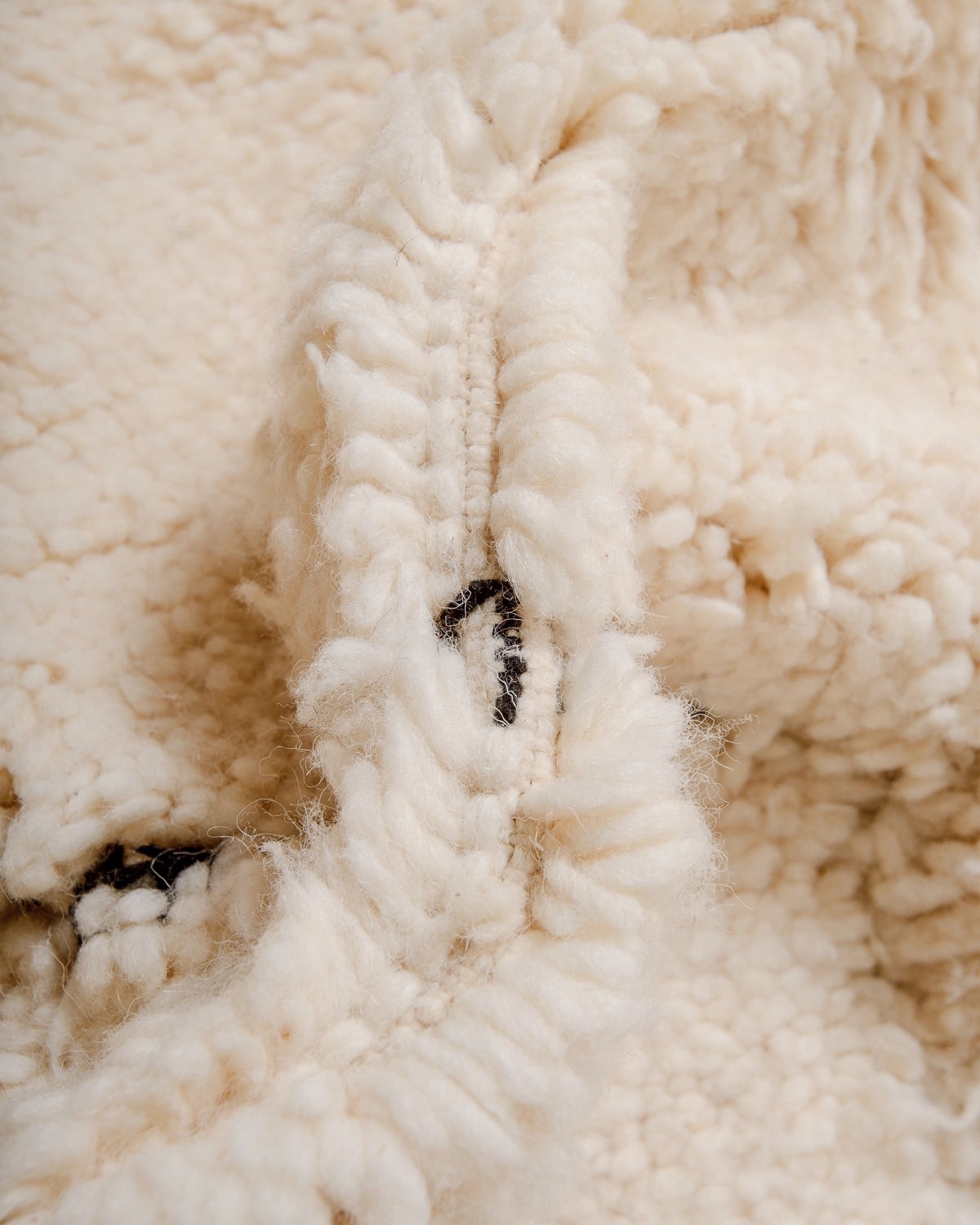 Detail of Berberlin Beniourain Rug made of cream wool with a subtle, abstract woven design in black.