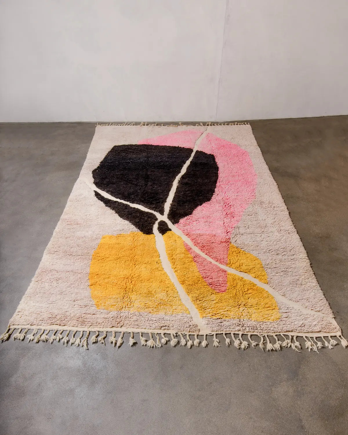 Handcrafted Berberlin Berber rug from Morocco featuring shades of pink, yellow, black and cream laying flat on concrete floor.