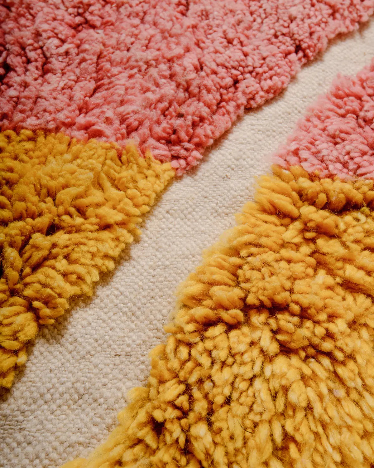 Detail of wool Berber rug featuring shades of pink and yellow with a flat woven design in natural wool. 