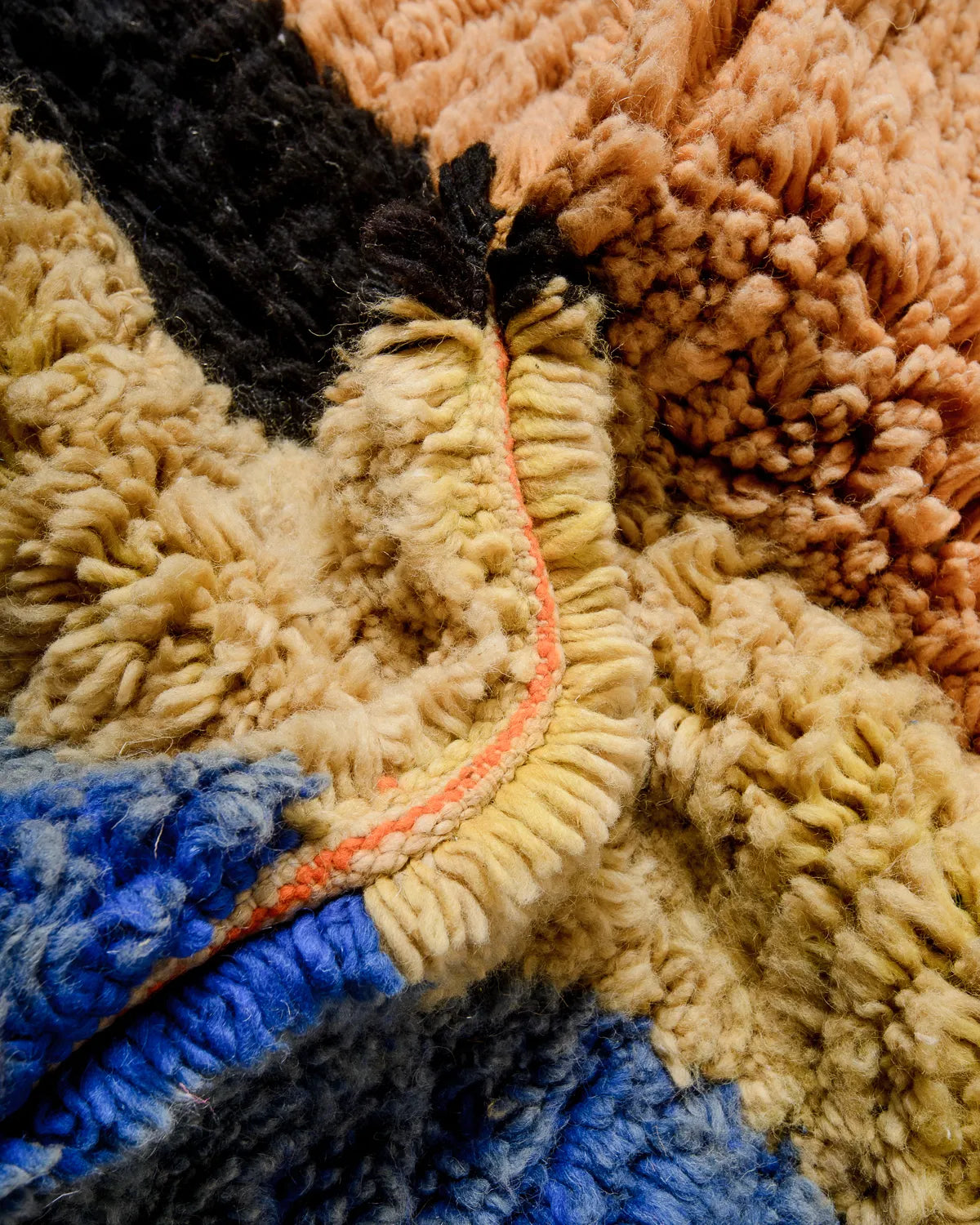 Detail of fluffy wool Berber rug in shades of yellow, apricot, blue and black.