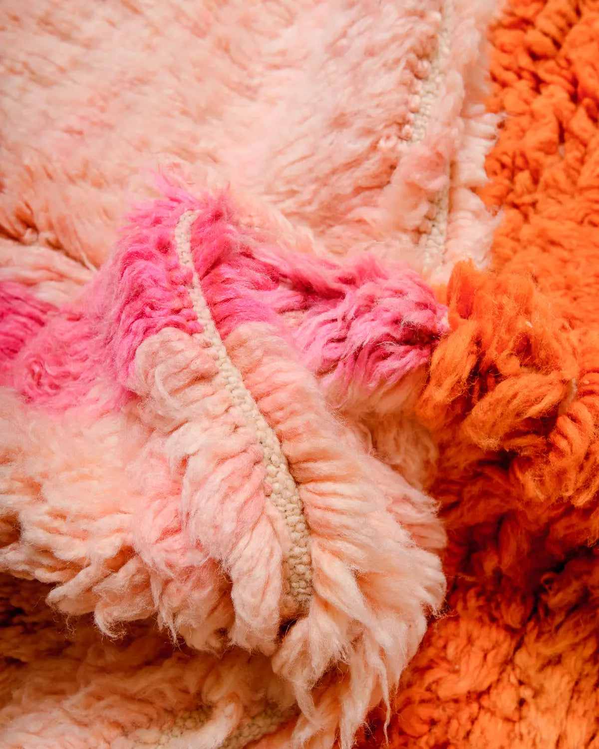 Close up of fluffy wool Berber rug in shades of peach, orange and pink.