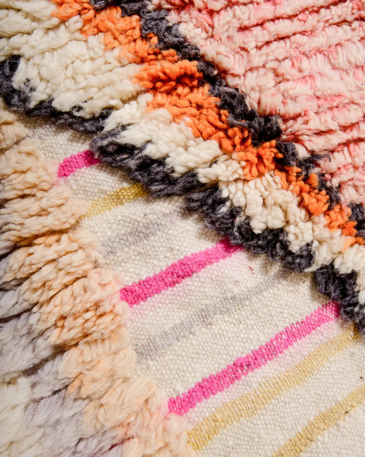 Detail of wool Berber rug in shades of cream, pink and orange, showing knotted and flat-woven areas. 