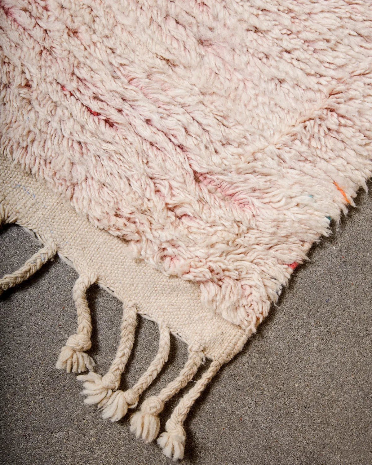 Tasseled edge of Berber rug made of pink fluffy wool laying on concrete floor.