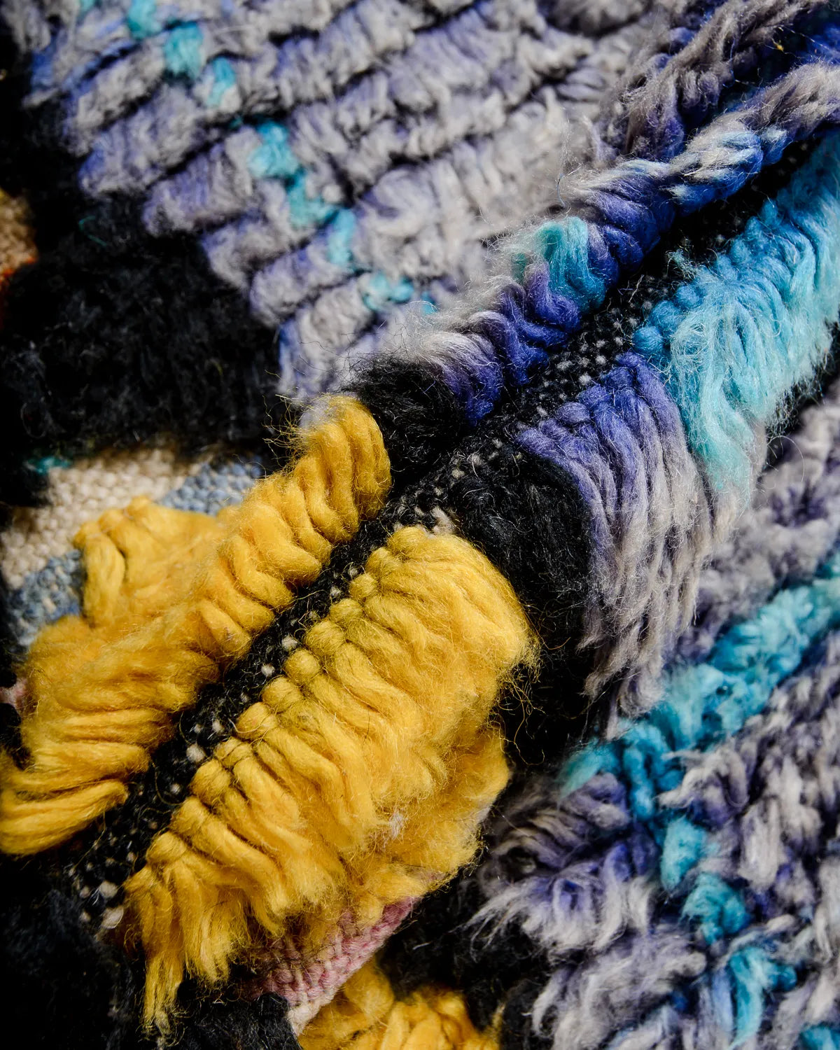 Detail of Berber rug made of fluffy wool in shades of blue, turquoise, yellow and black.