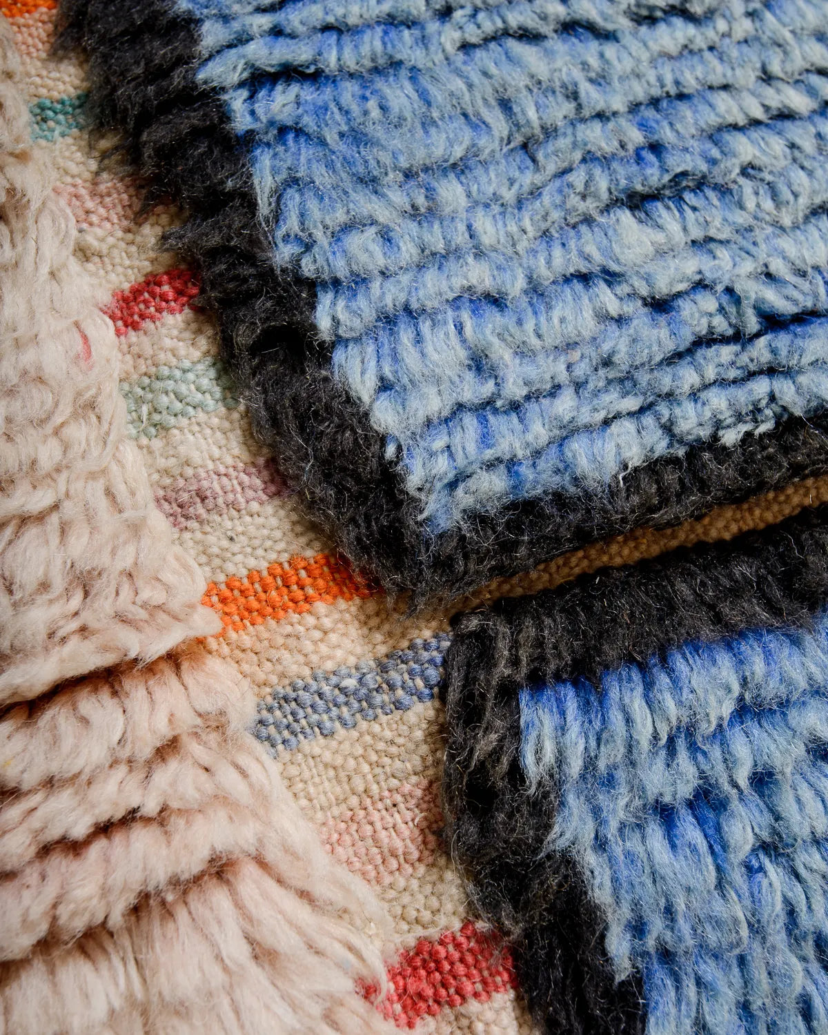 Detail of Berber rug made of fluffy wool in shades of blue and black with a striped flat-woven base.