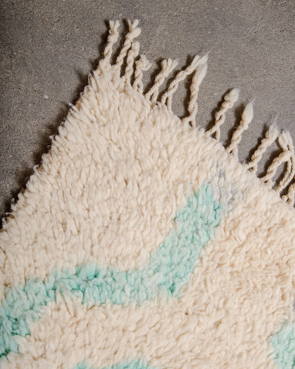 Natural wool tassels on a Berberlin Vintage Berber Rug made of fluffy cream and turquoise wool, laying on grey concrete.