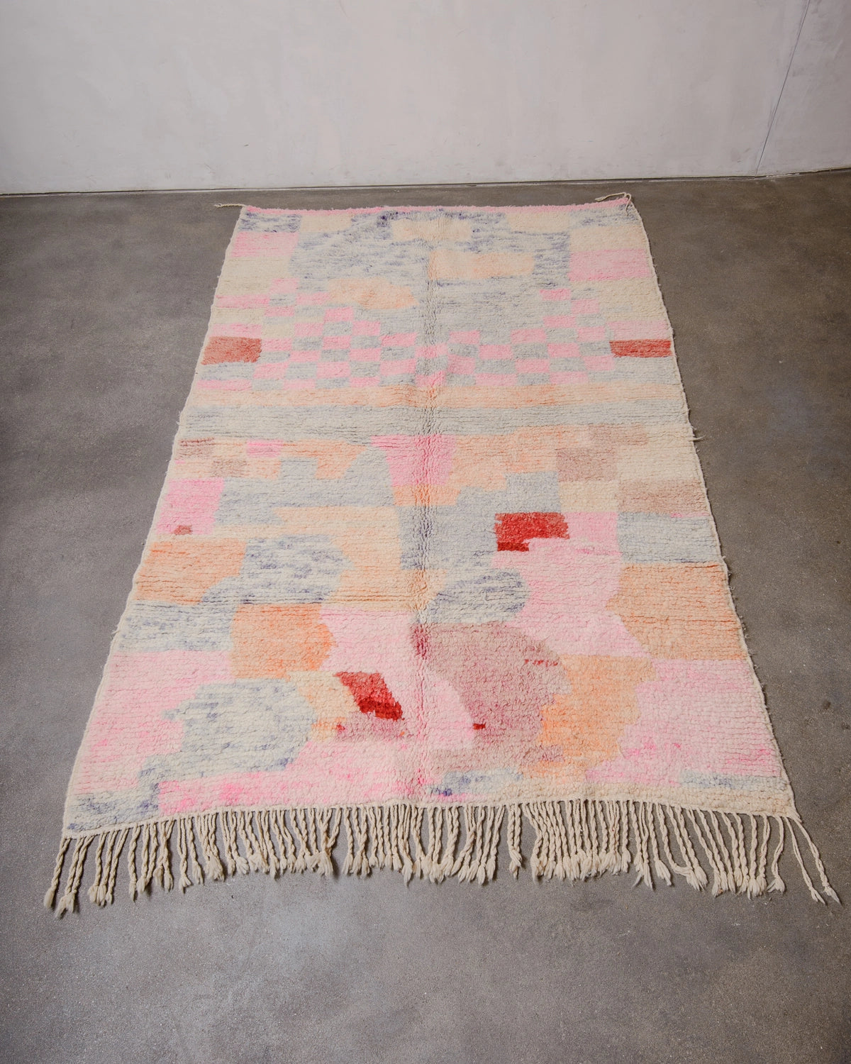 Berberlin Vintage Berber Rug made of fluffy wool in pink, apricot and lavender laying flat on concrete floor.