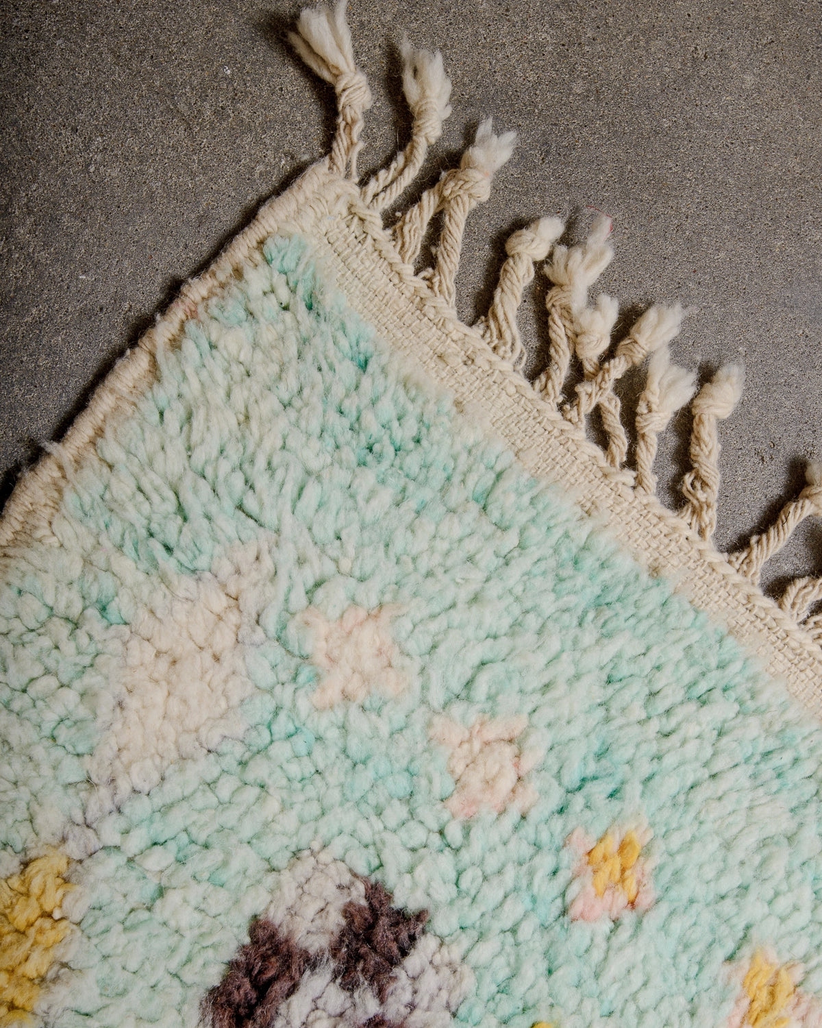 Natural wool tassels on Berberlin Vintage Berber Rug made of fluffy turquoise wool, laying on grey concrete floor.