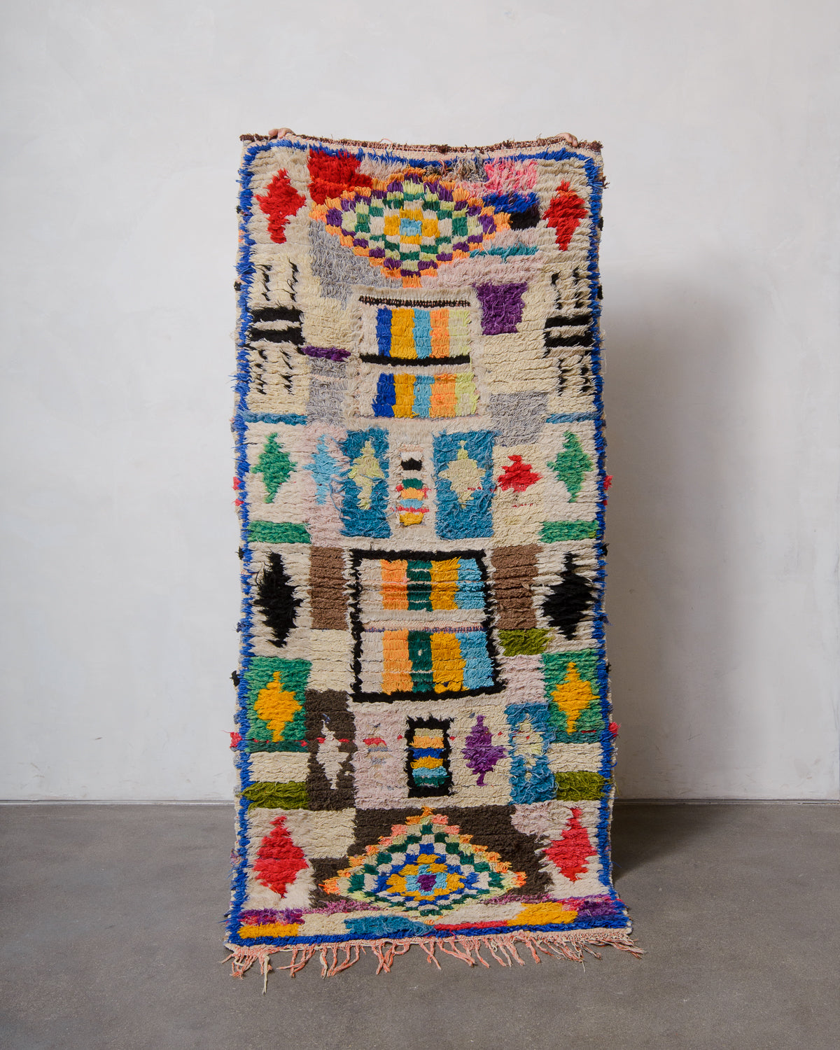 Colourful Boucherouite runner rug being held up in front of a white wall. 