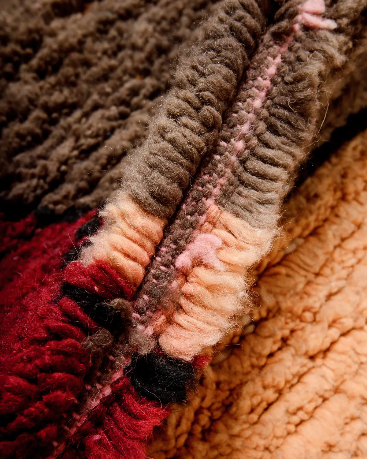 Close up of brown, apricot and red wool in a rug.