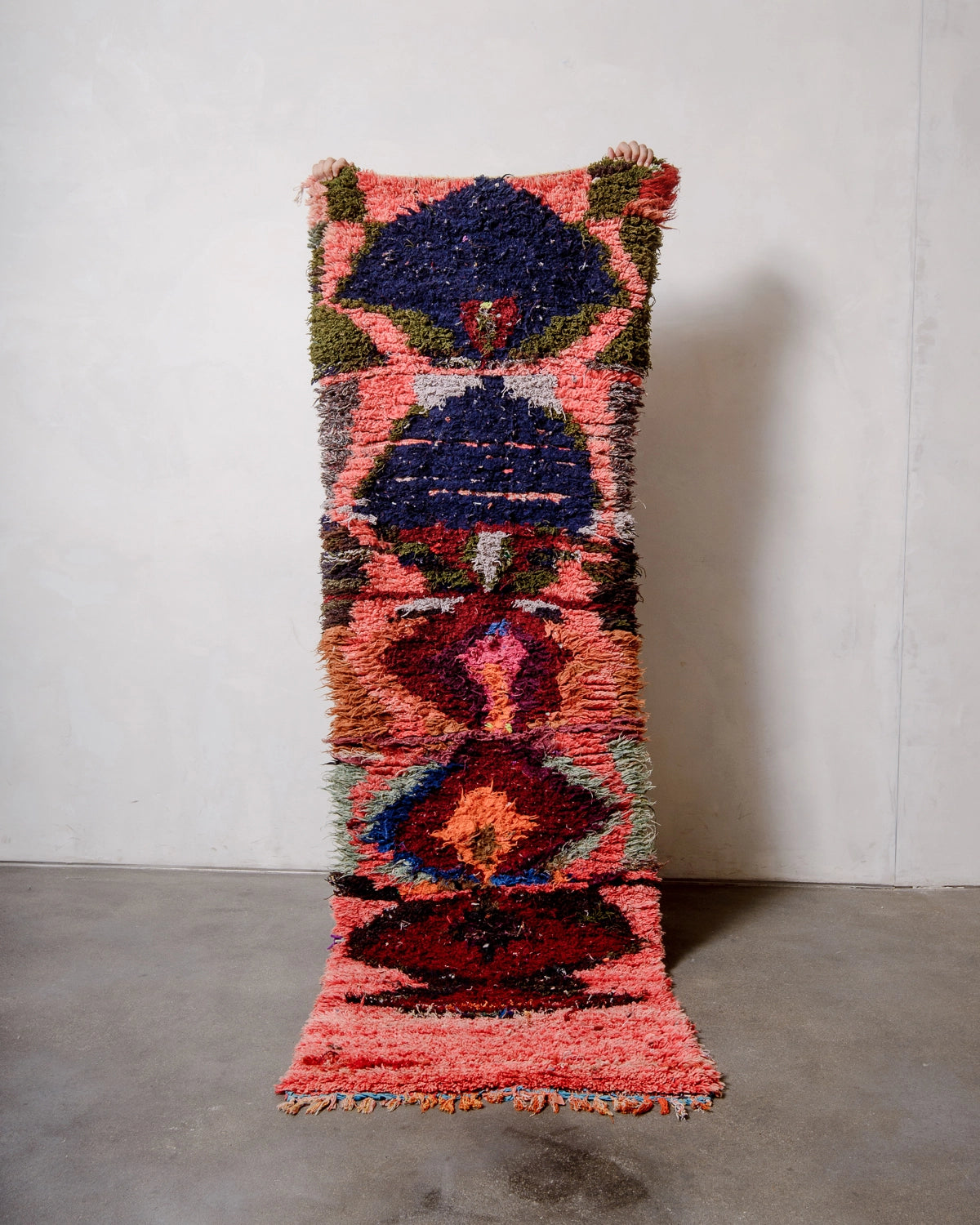 Berberlin Vintage Berber Rug in shades of red, pink, navy, khaki, burgundy held up against a white. 