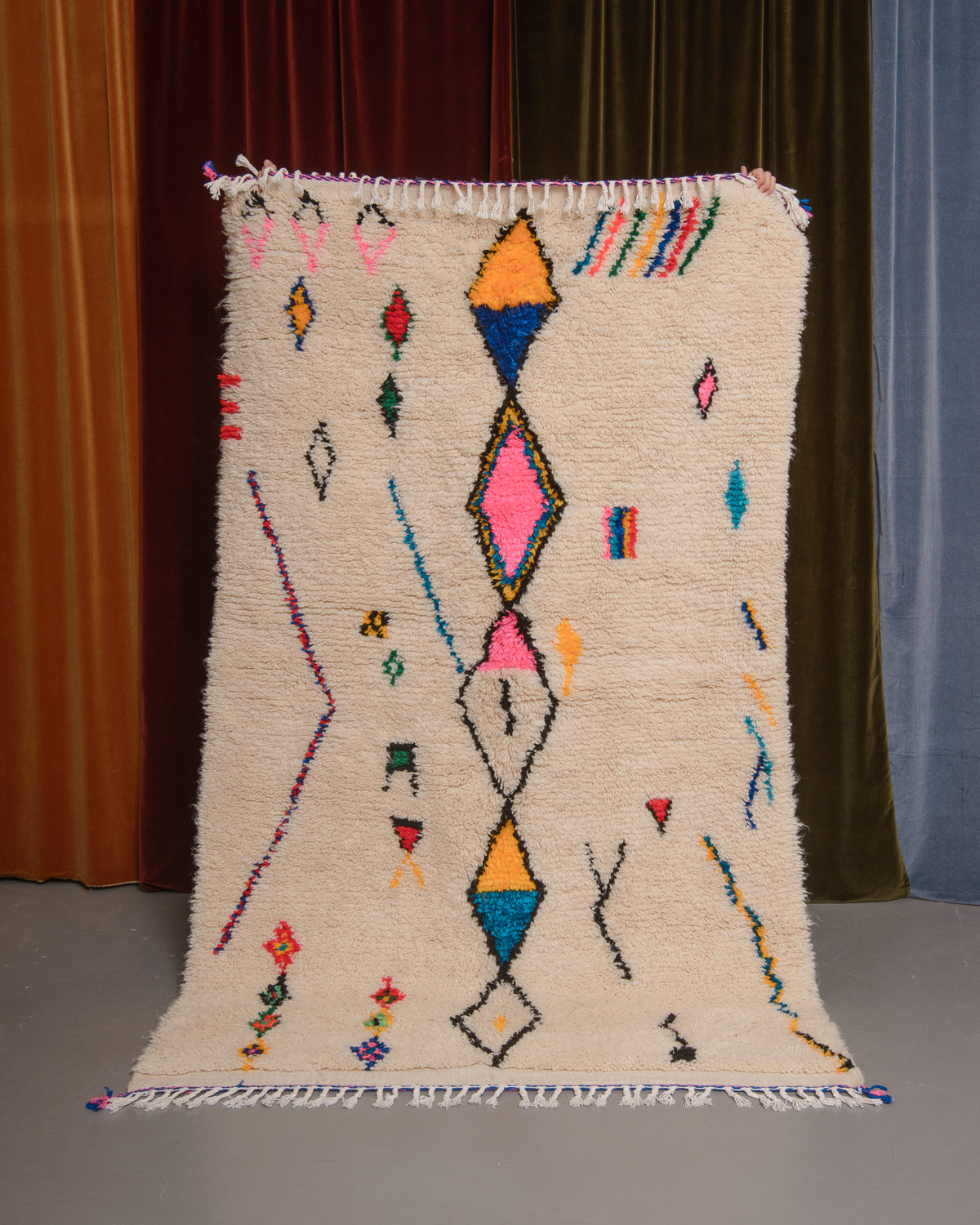 Azilal rug held in front of velvet curtains. 