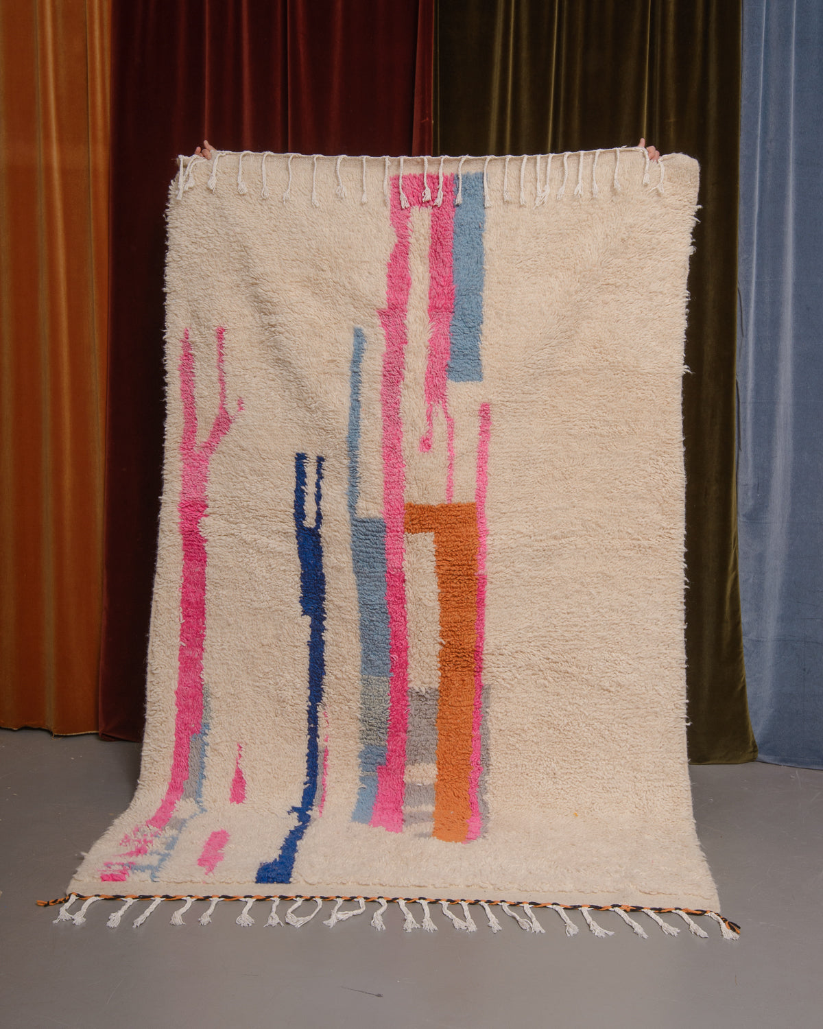 Azilal rug held in front of velvet curtains. 