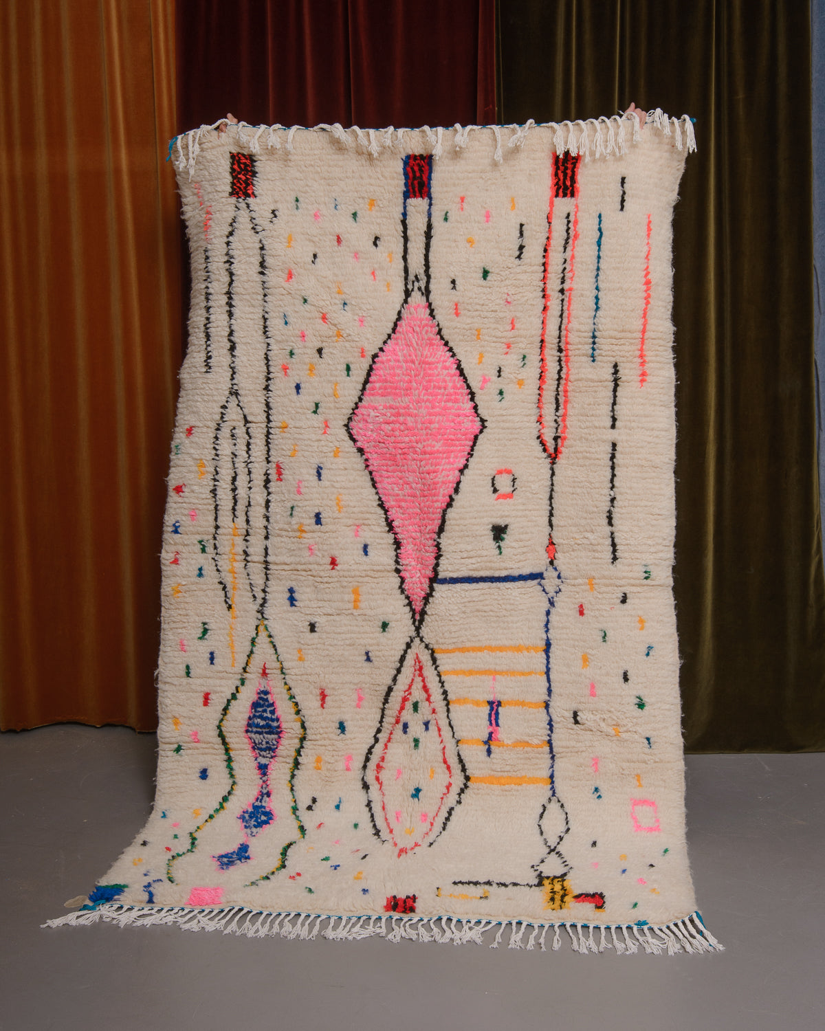 Azilal rug held in front of velvet curtains. 