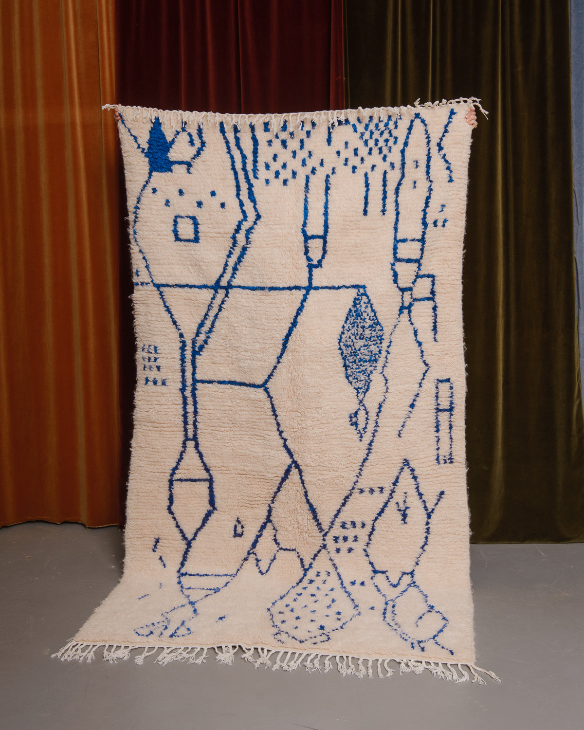 Azilal rug held in front of velvet curtains. 