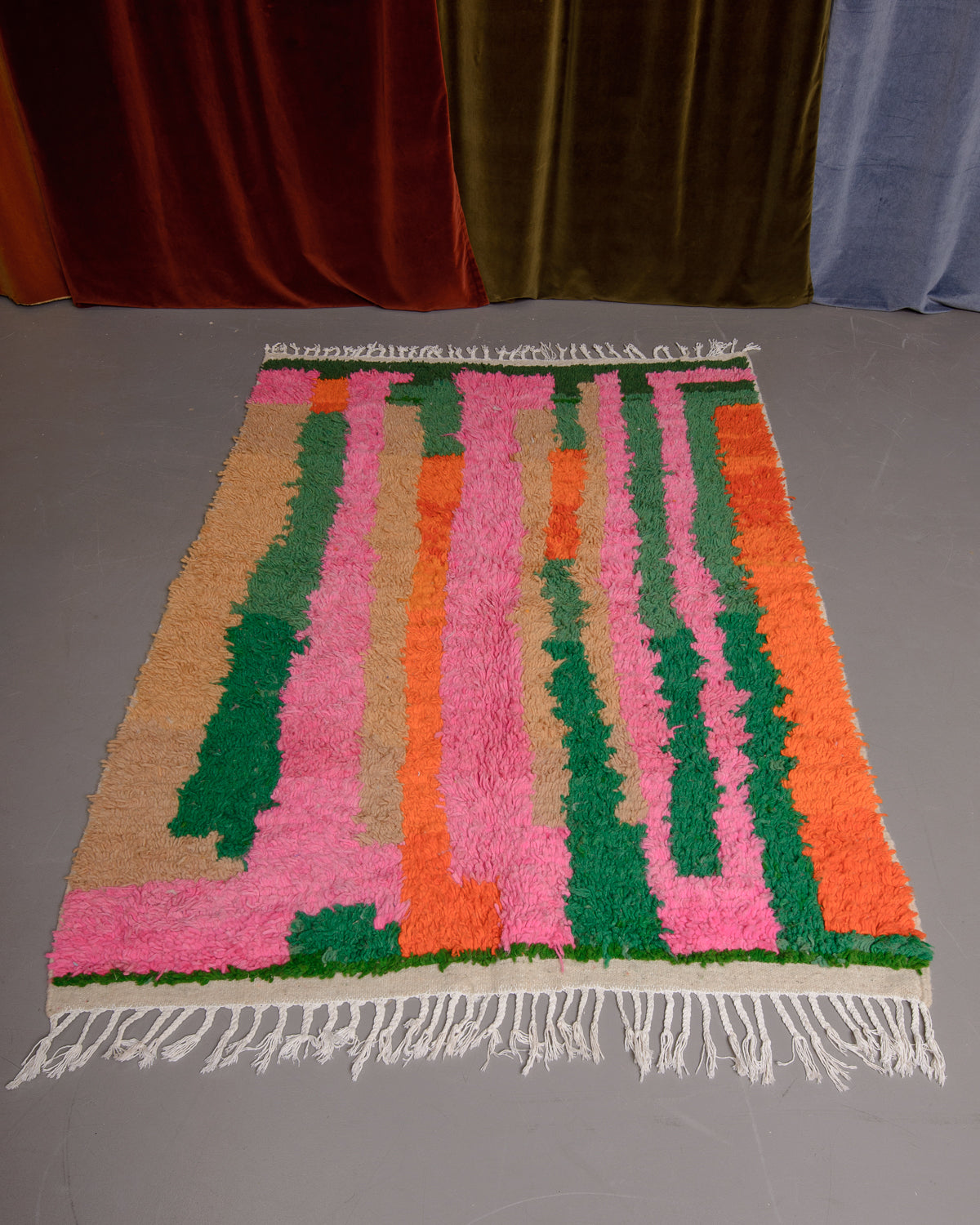 Azilal rug featuring colourful design on a grey floor in front of curtains.