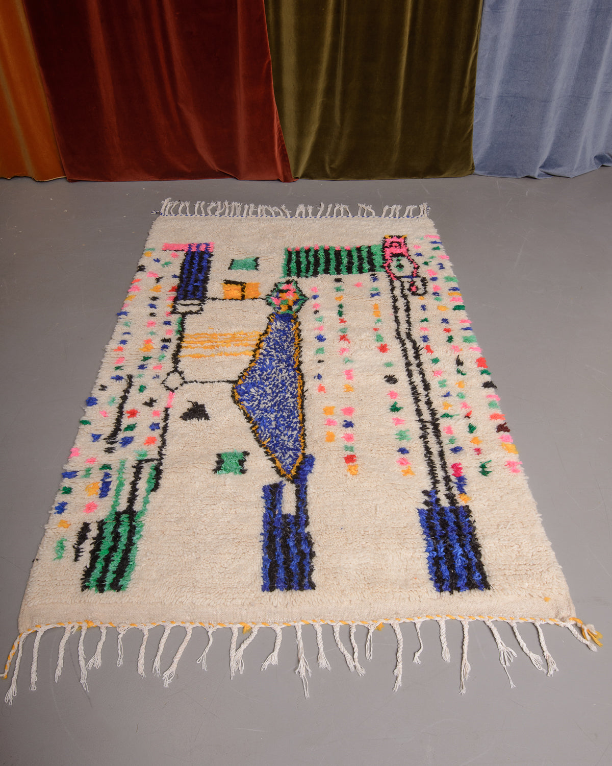 Azilal rug featuring colourful design on a grey floor in front of curtains.