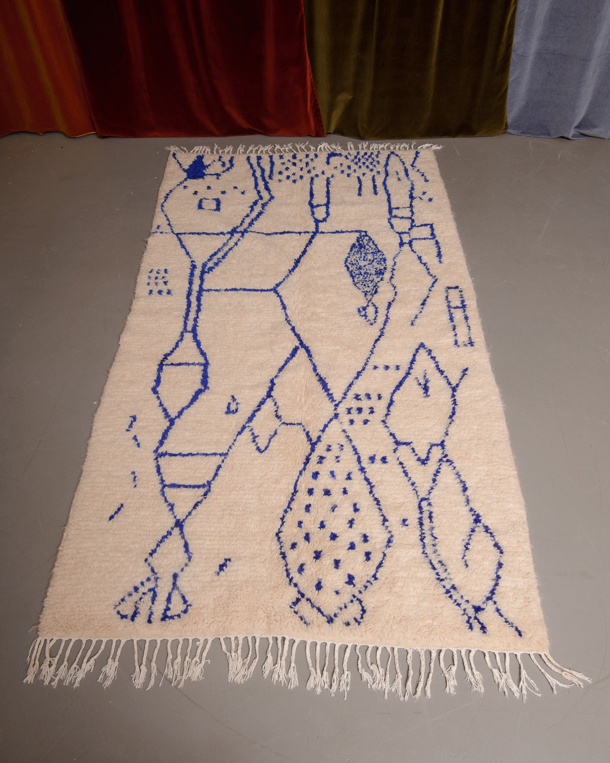 Azilal rug featuring colourful design on a grey floor in front of curtains.