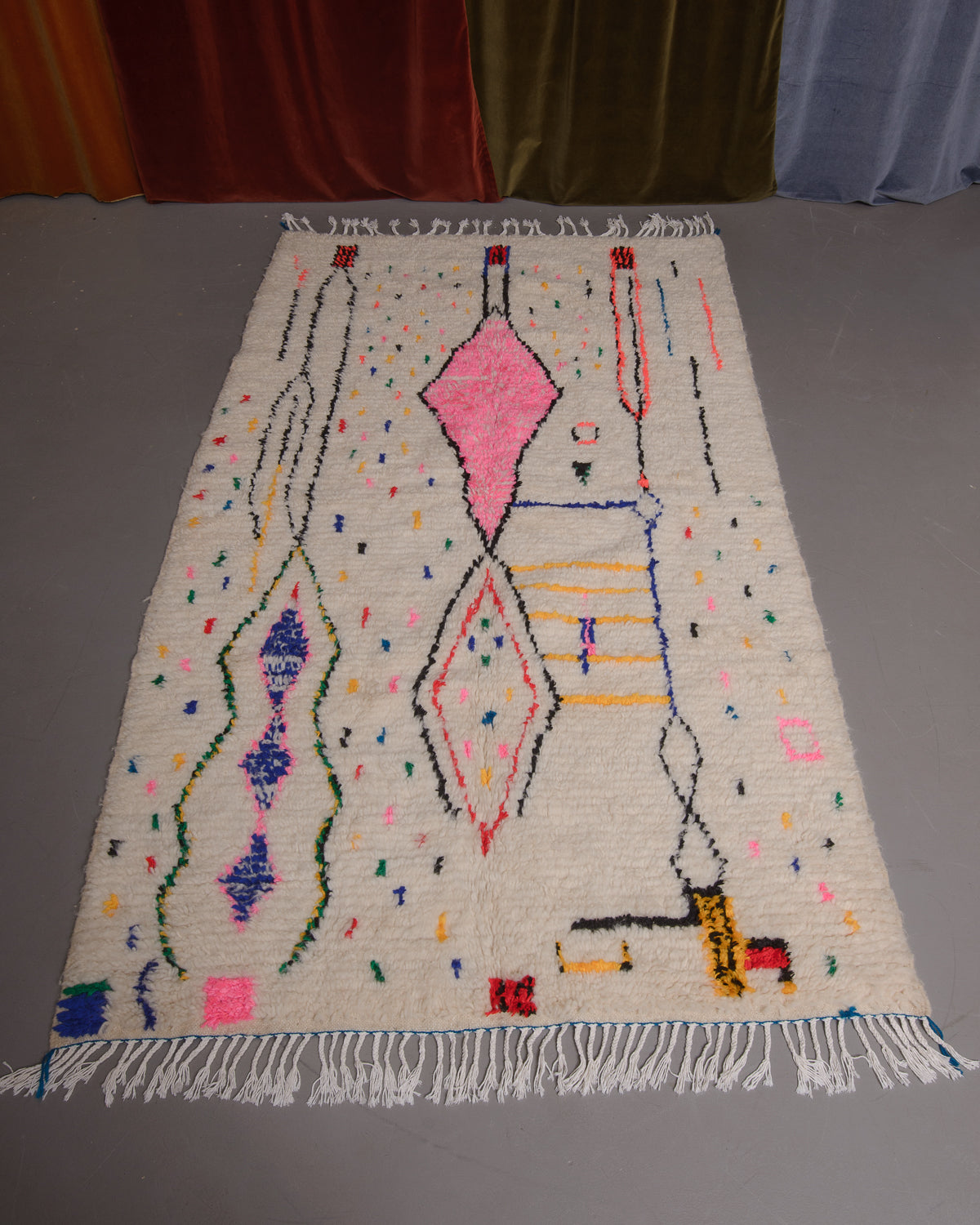 Azilal rug featuring colourful design on a grey floor in front of curtains.