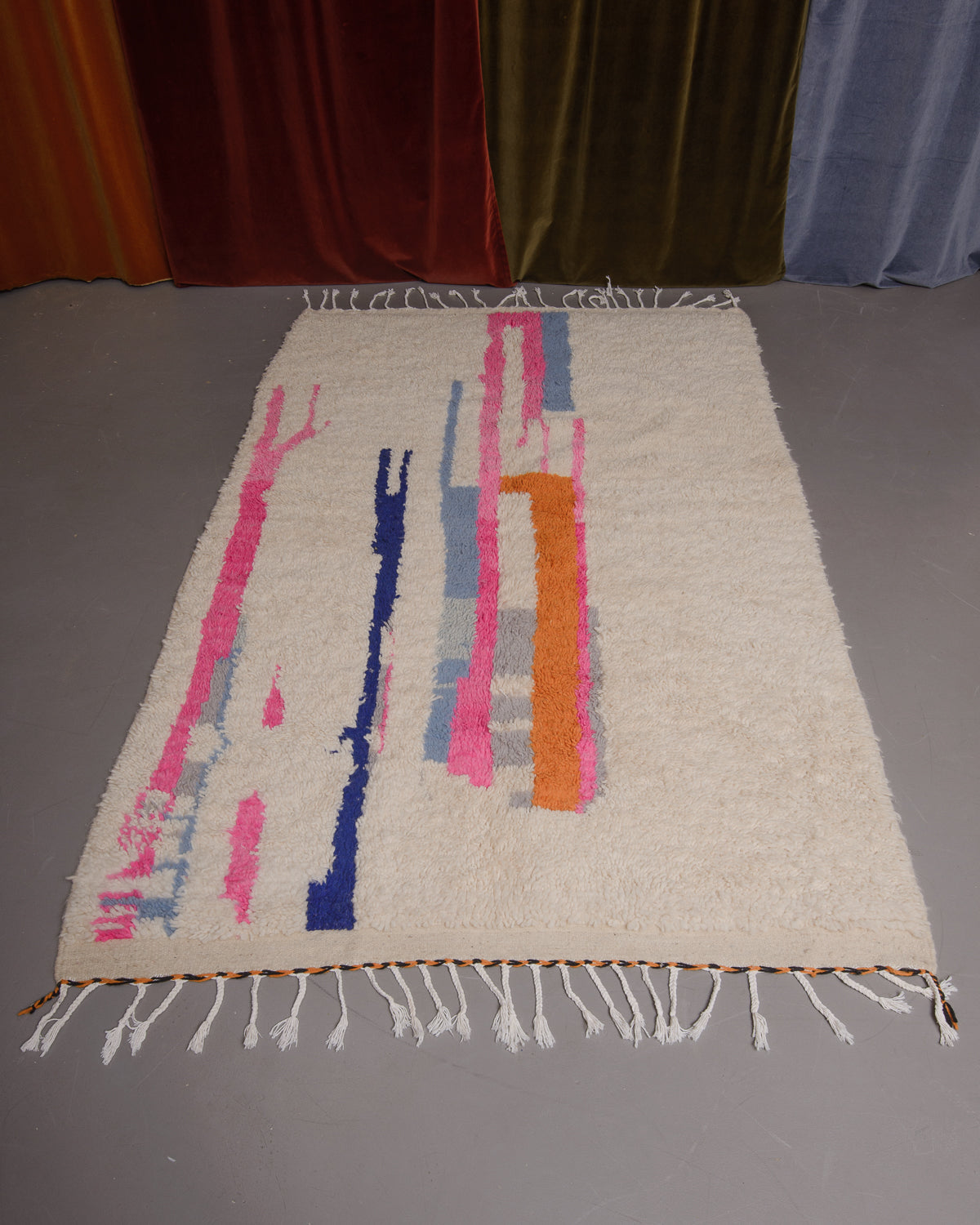 Azilal rug featuring colourful design on a grey floor in front of curtains.