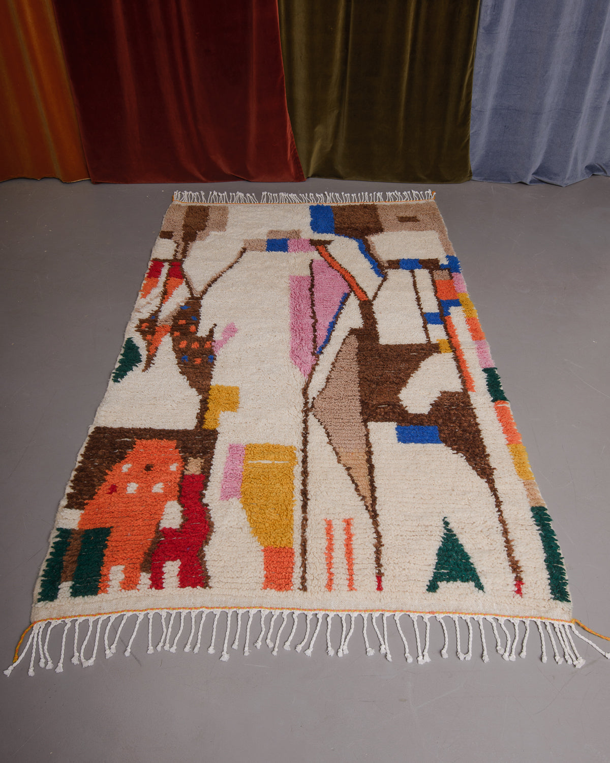 Azilal rug featuring colourful design on a grey floor in front of curtains.