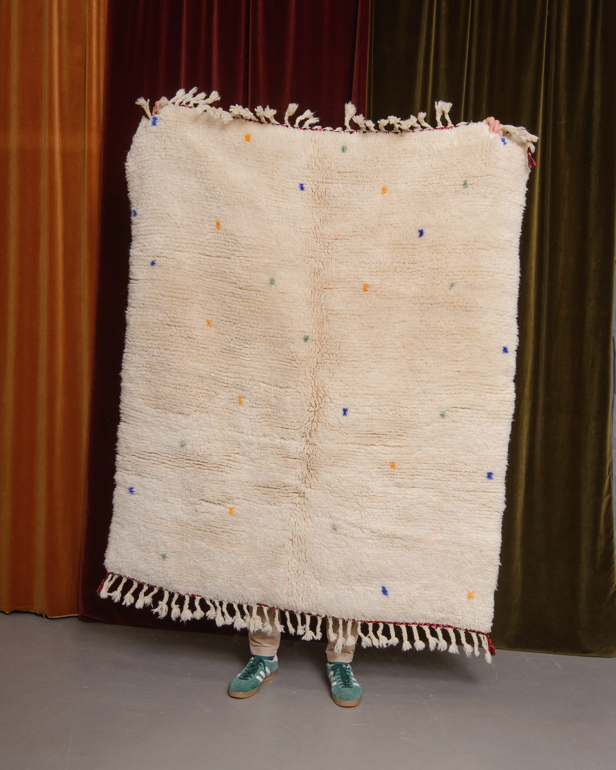 Cream wool rug being held up in front of velvet curtains.