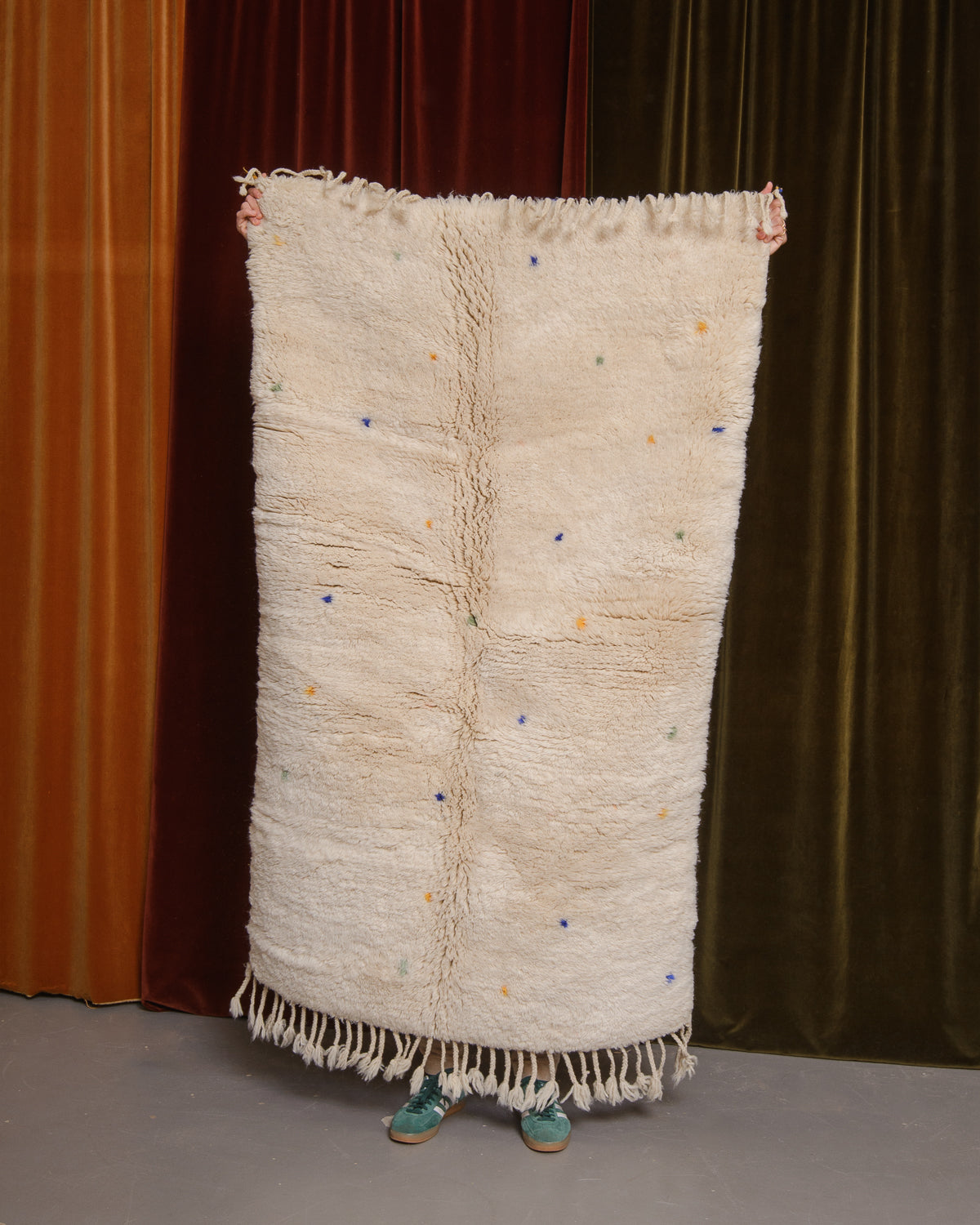 Cream wool rug being held up in front of velvet curtains.