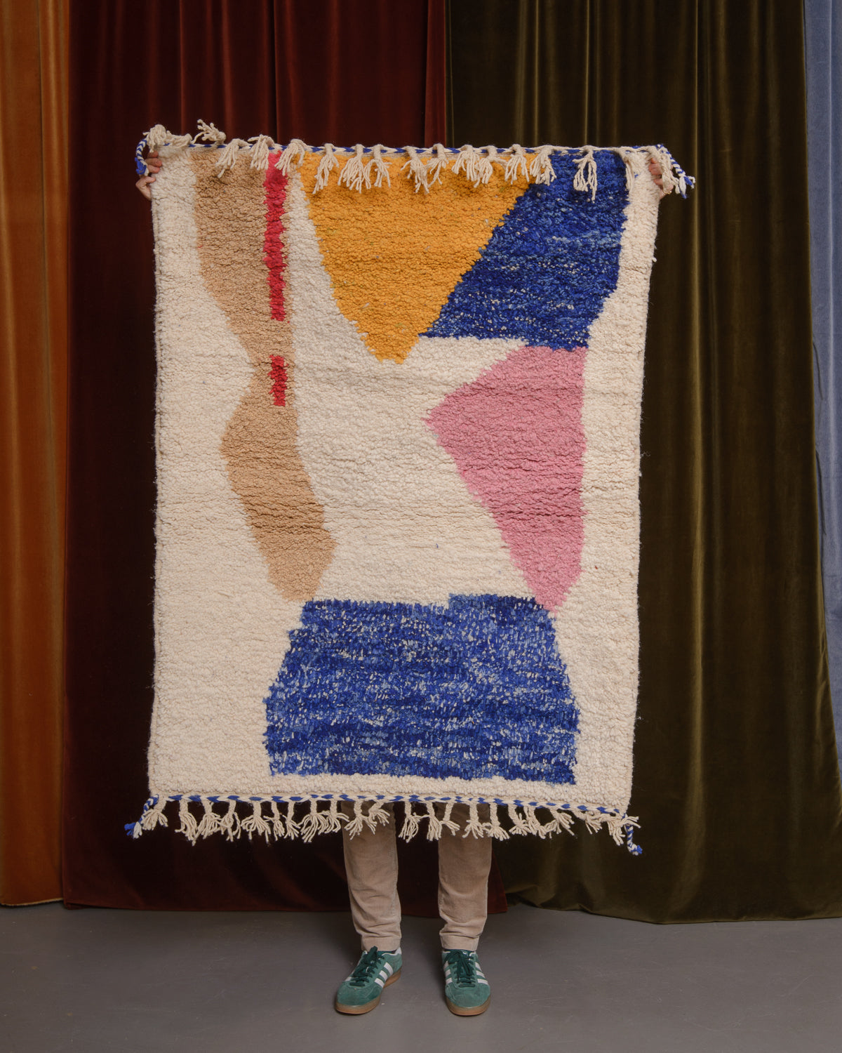 Berberlin Special Edition Beniourain rug held up in front of a velvet curtain.