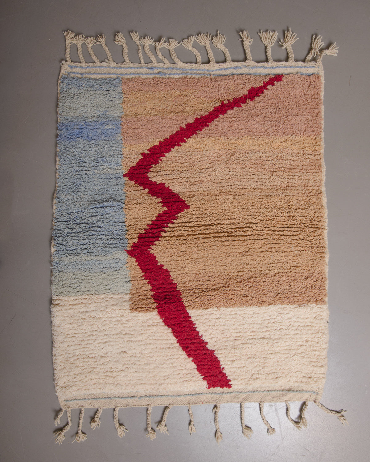 Wool rug with cream tassels on a grey floor.