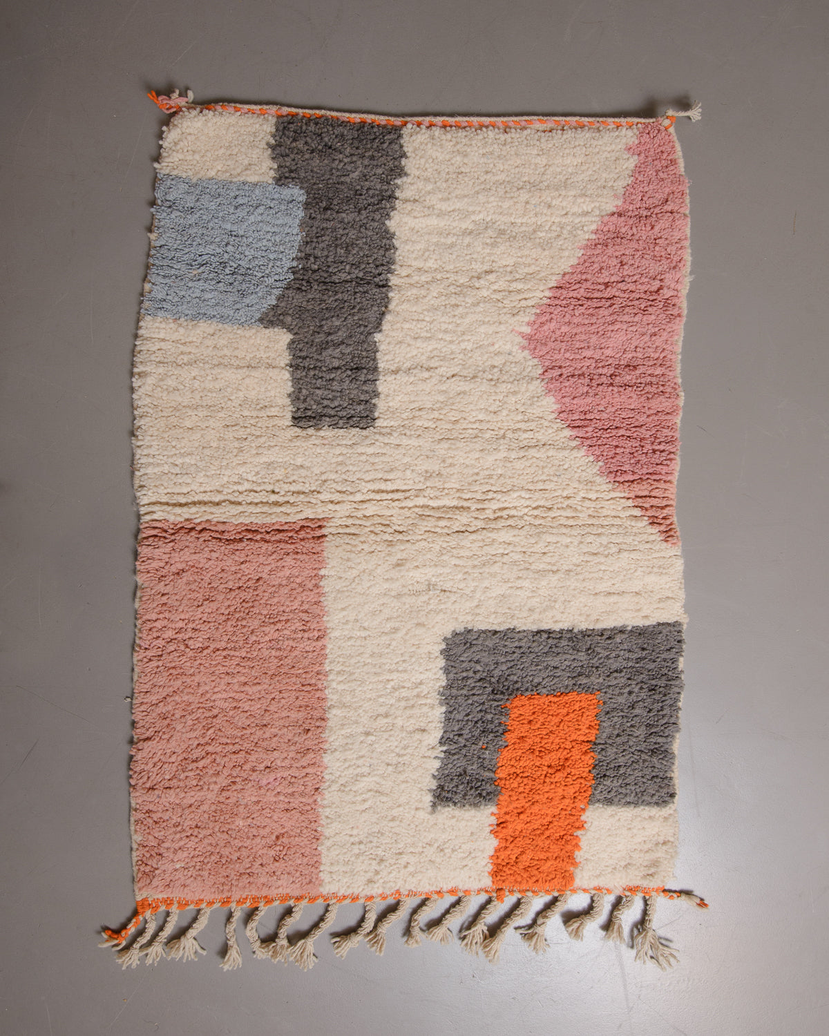 Grey and blue rug with cream tassels on one end, on a grey floor.