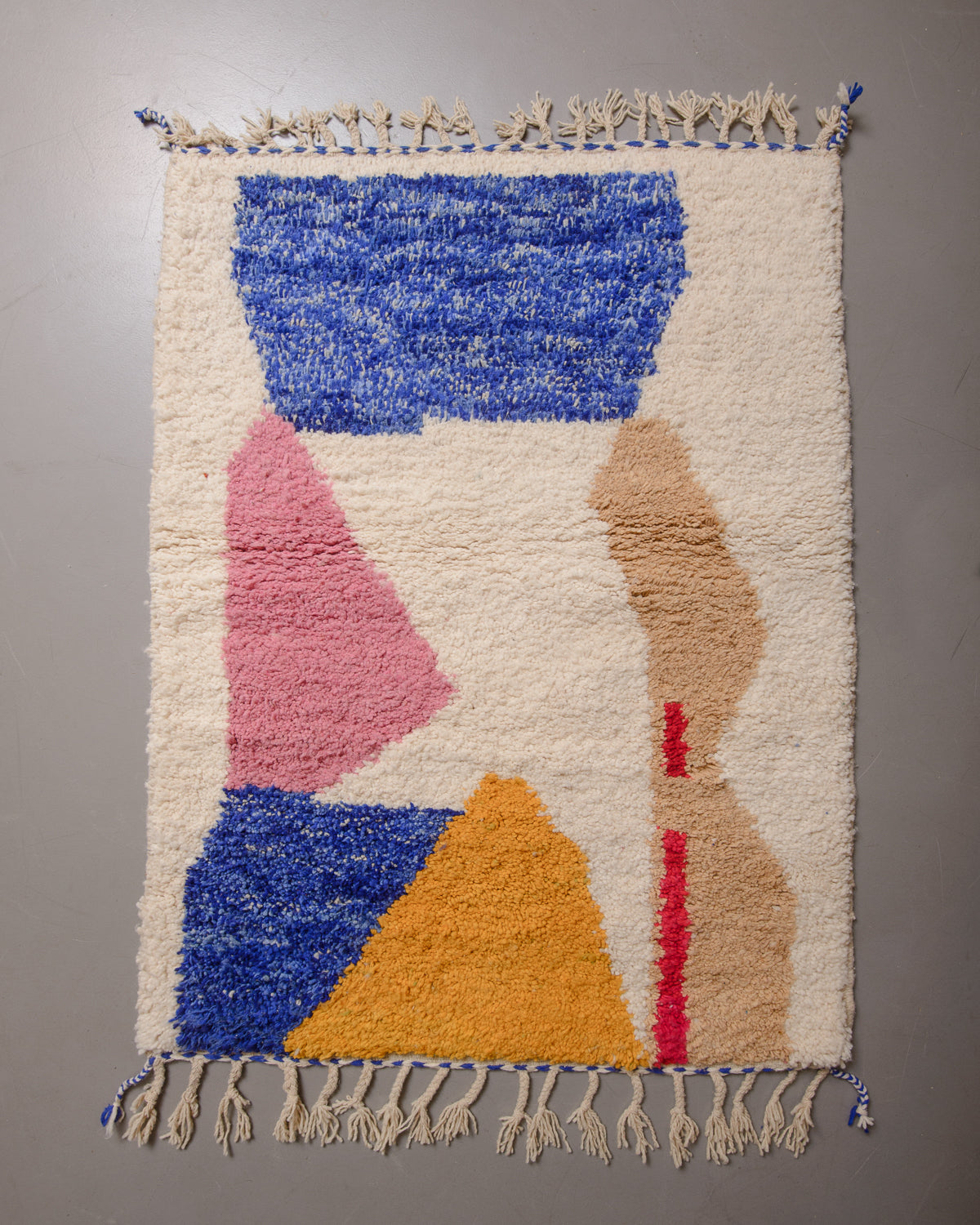 Wool rug with cream tassels on a grey floor.