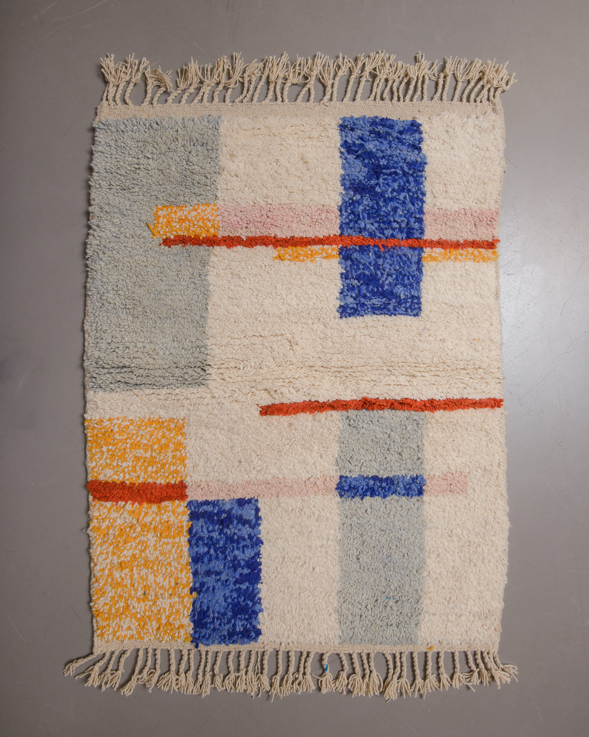 Wool rug with cream tassels on a grey floor.