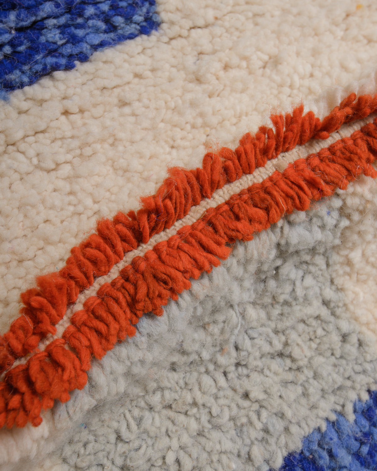 Close up of cream wool rug with blue. rust orange and grey details. 