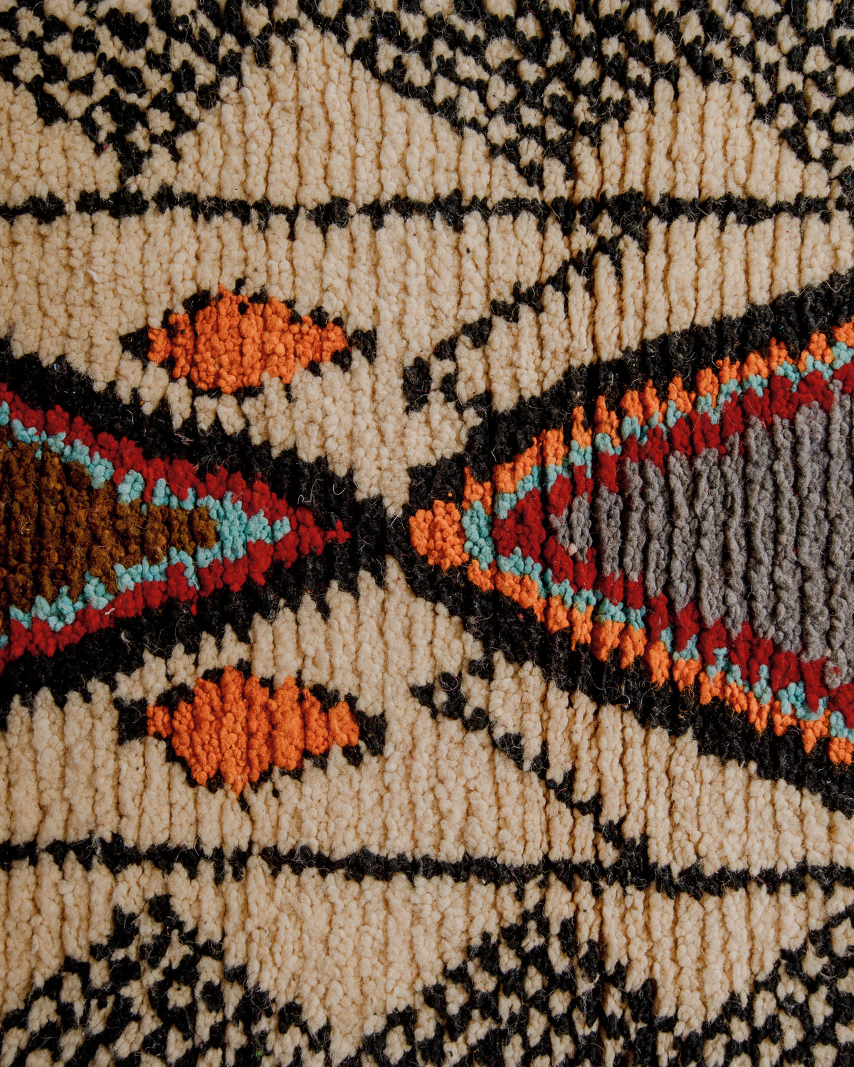Surface of wool boujaad rug in beige, black, red, turquoise an orange.