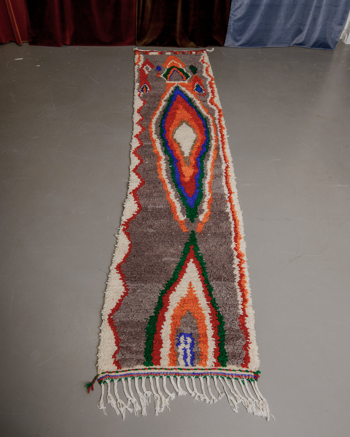 Vintage Berberlin boujaad runner rug on grey floor in front of velvet curtains.